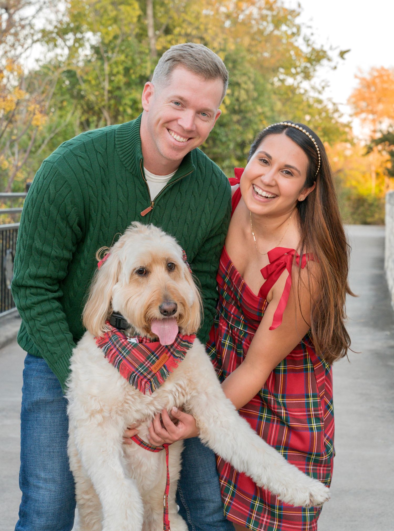 Smiling couple holding their fluffy dog wearing a plaid bandana during a fall portrait session.
