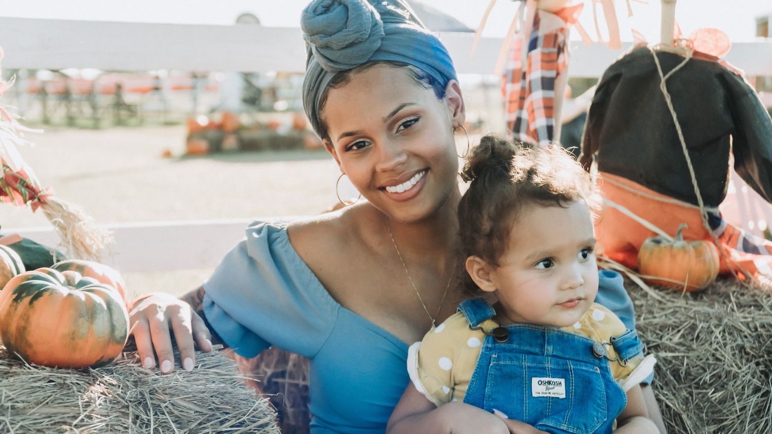 Mother and young child sitting on hay bales at a pumpkin patch, smiling during an outdoor fall portrait.