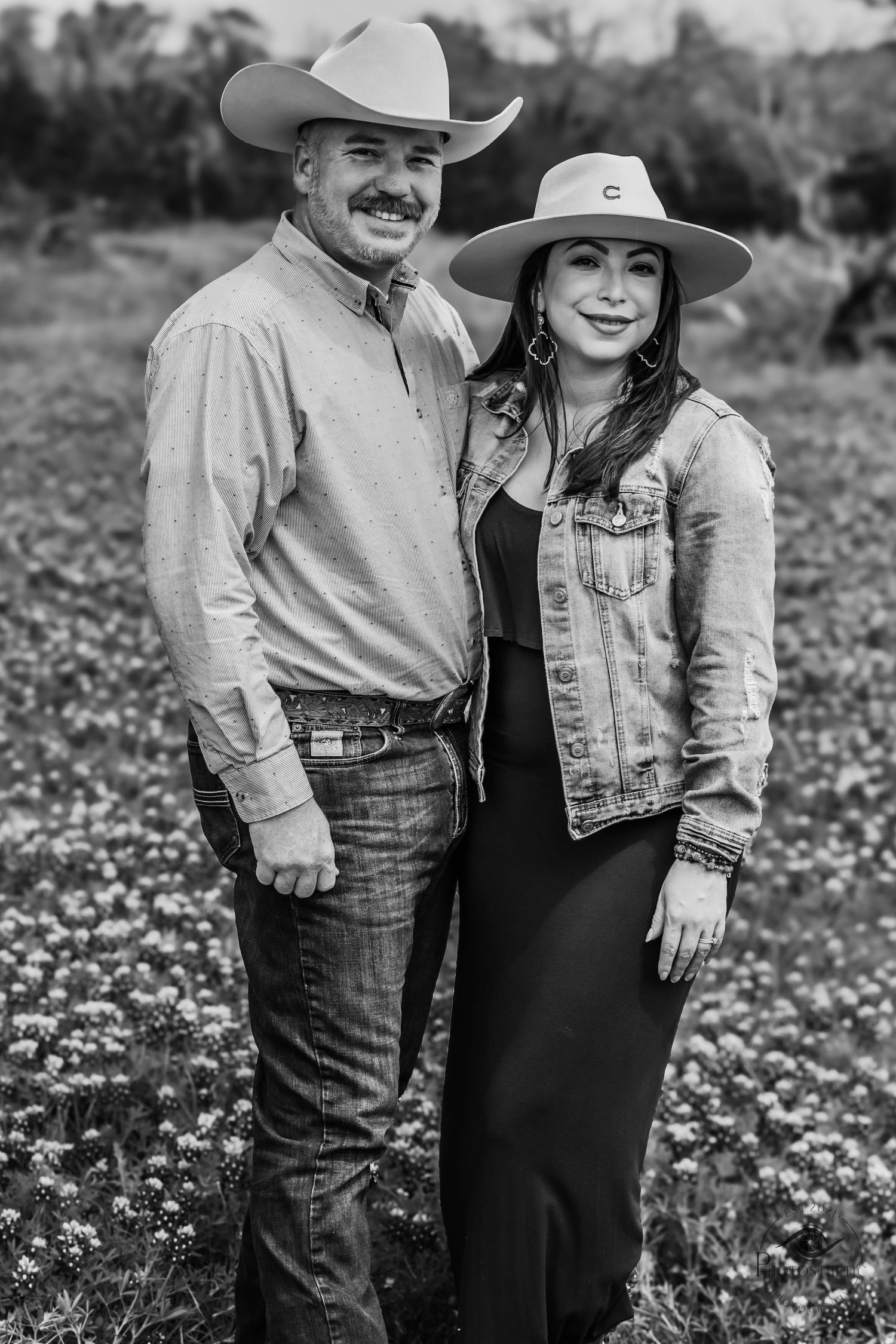 Black and white portrait of a couple wearing cowboy hats standing together in a wildflower field.
