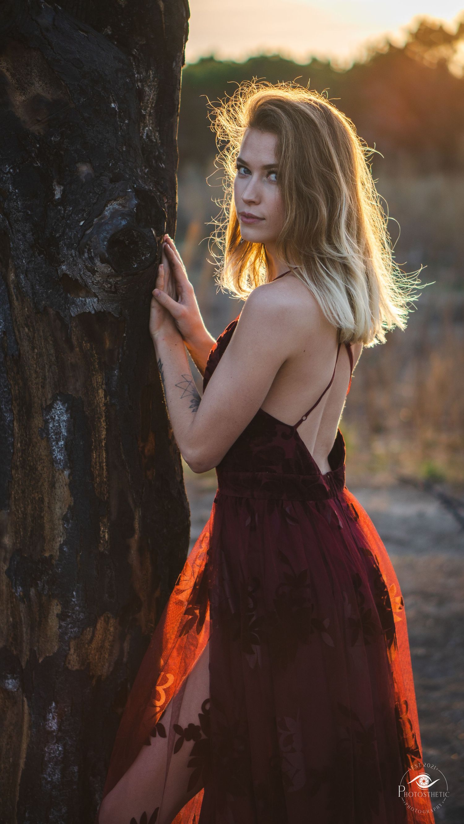 Woman with tattoos posing outdoors at sunset, surrounded by soft colored smoke and warm natural light.