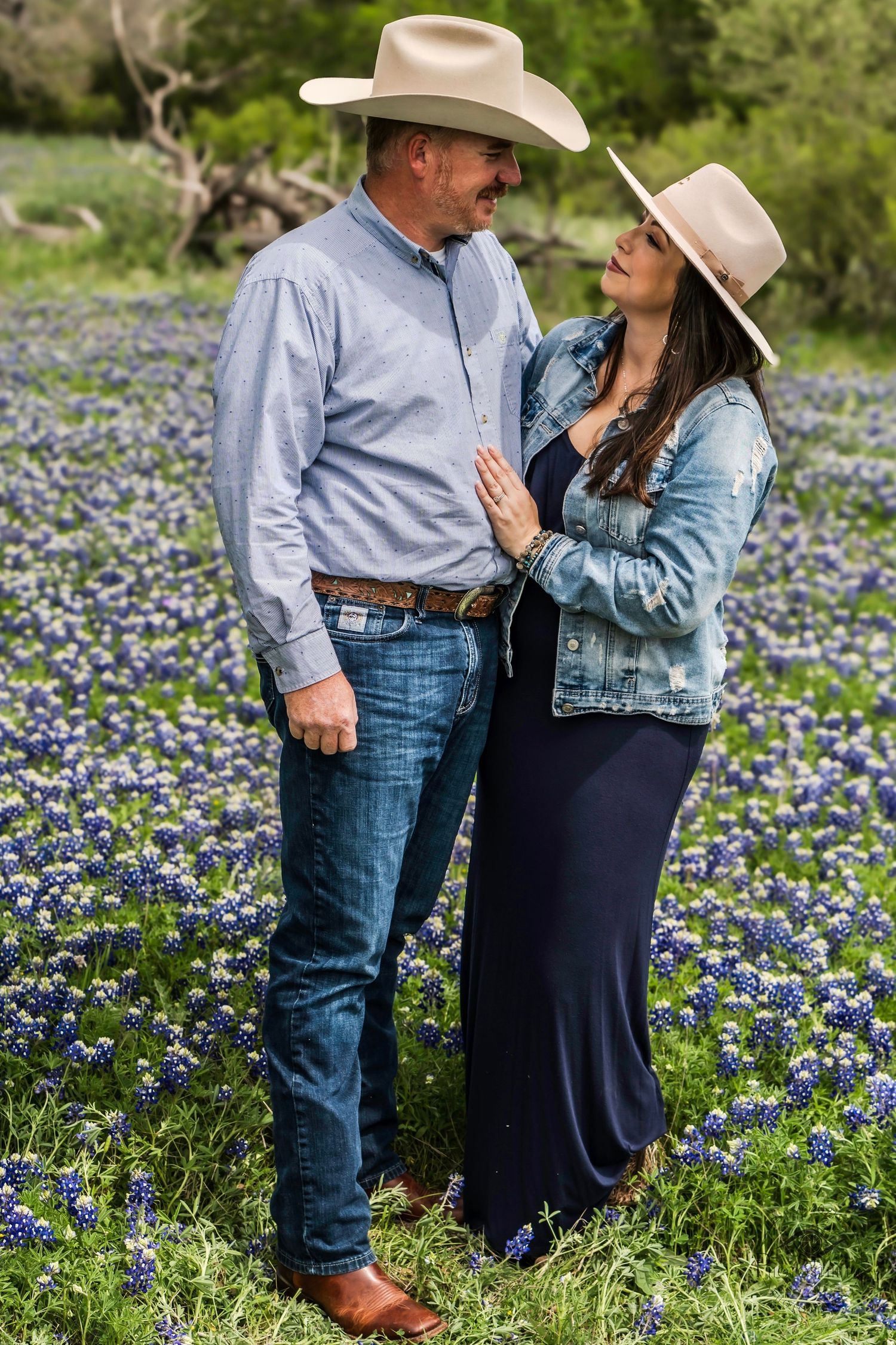 Couple wearing cowboy hats standing together in a bluebonnet field during a natural light portrait.