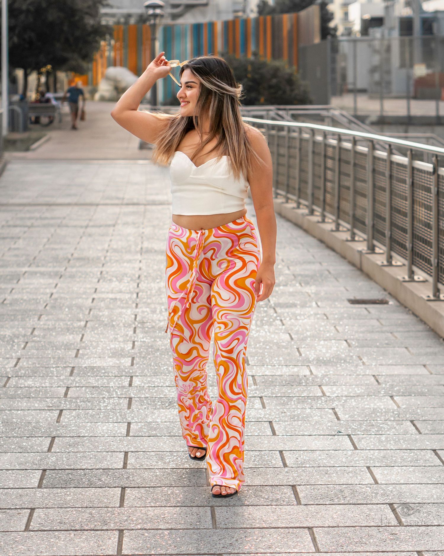 Woman walking confidently along a city walkway wearing patterned pants and a sleeveless top