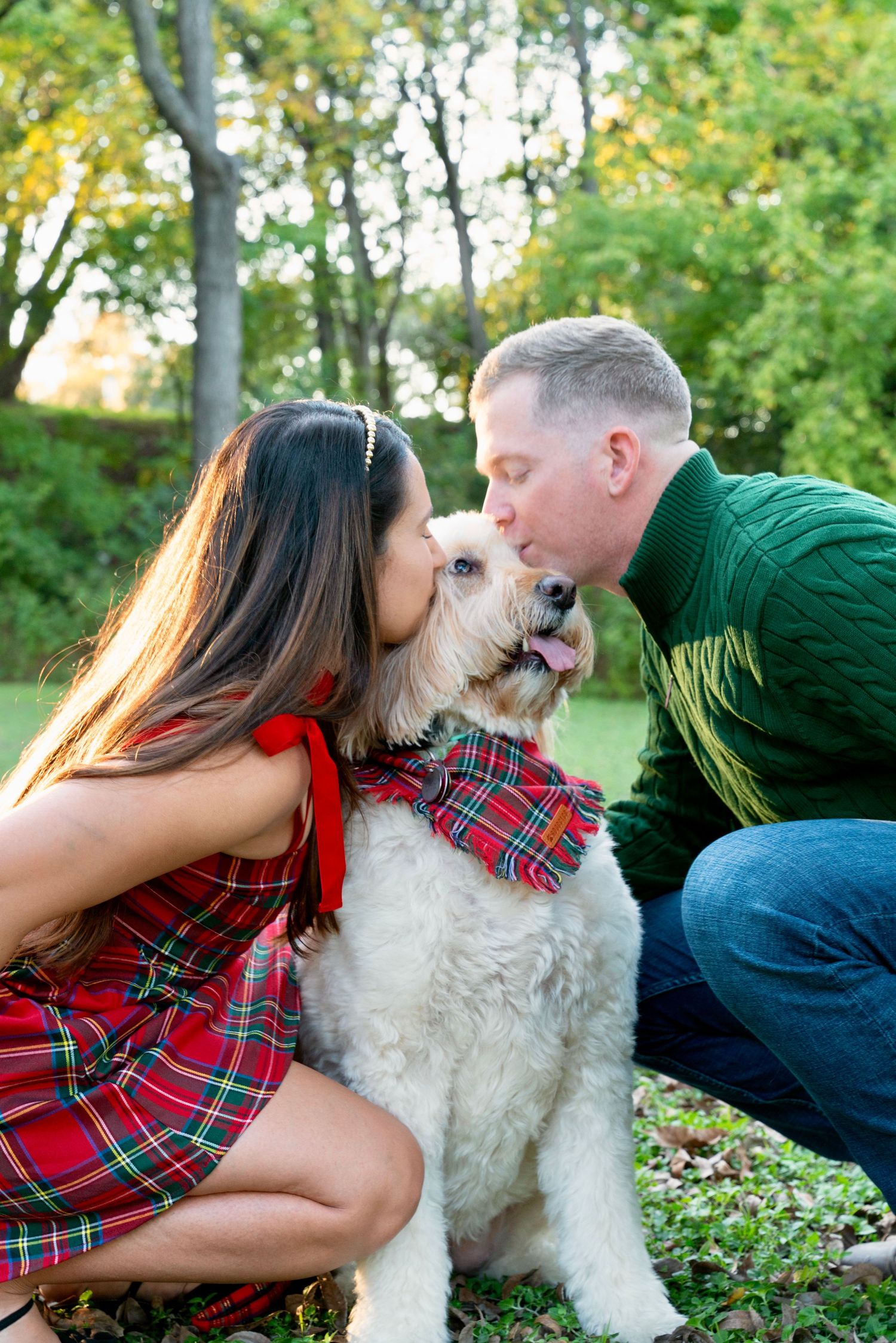 Couple kissing their dog outdoors in a park during a fall portrait session.