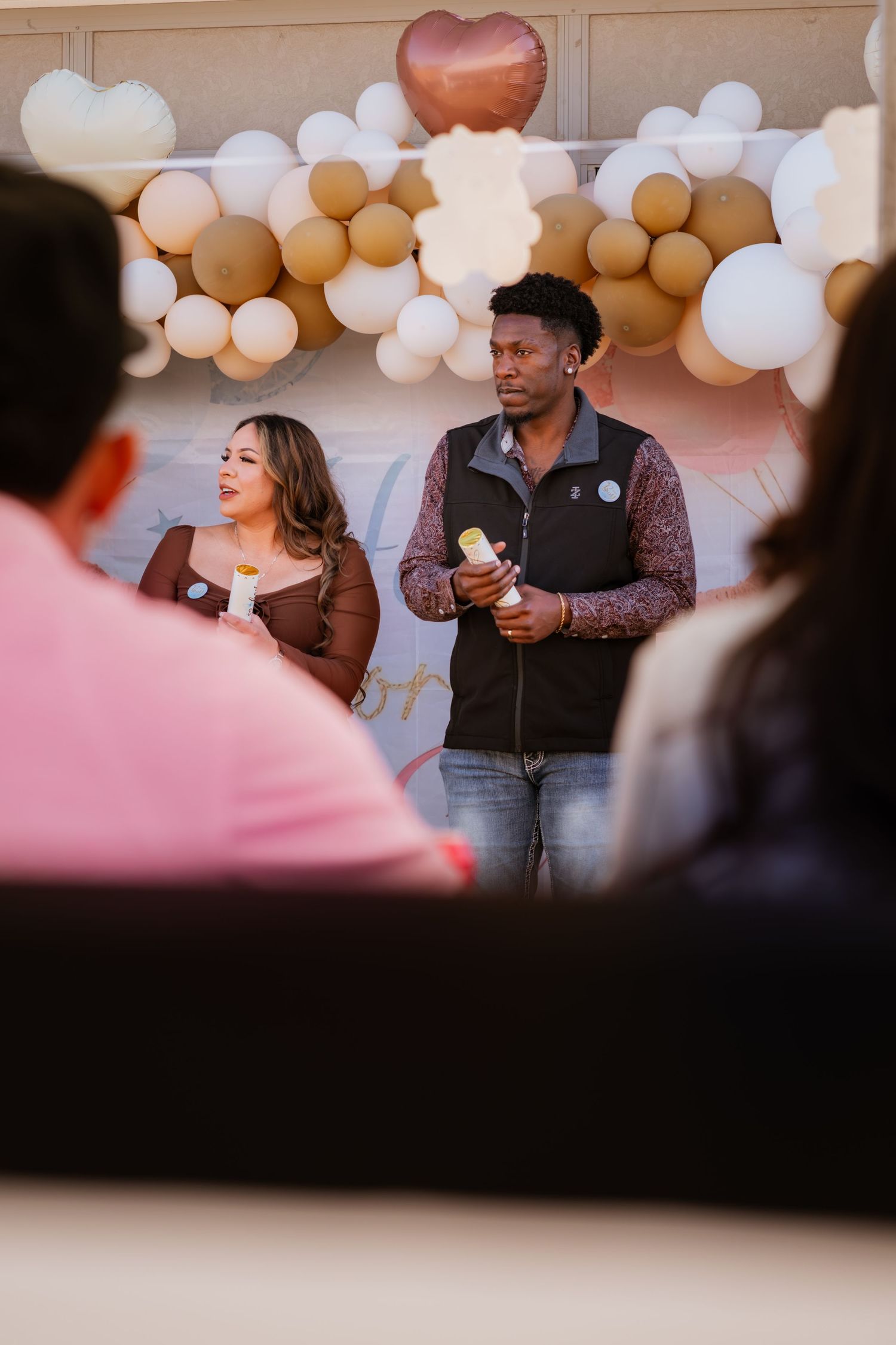 People gather at a celebration with pink and white balloon decorations in the background.