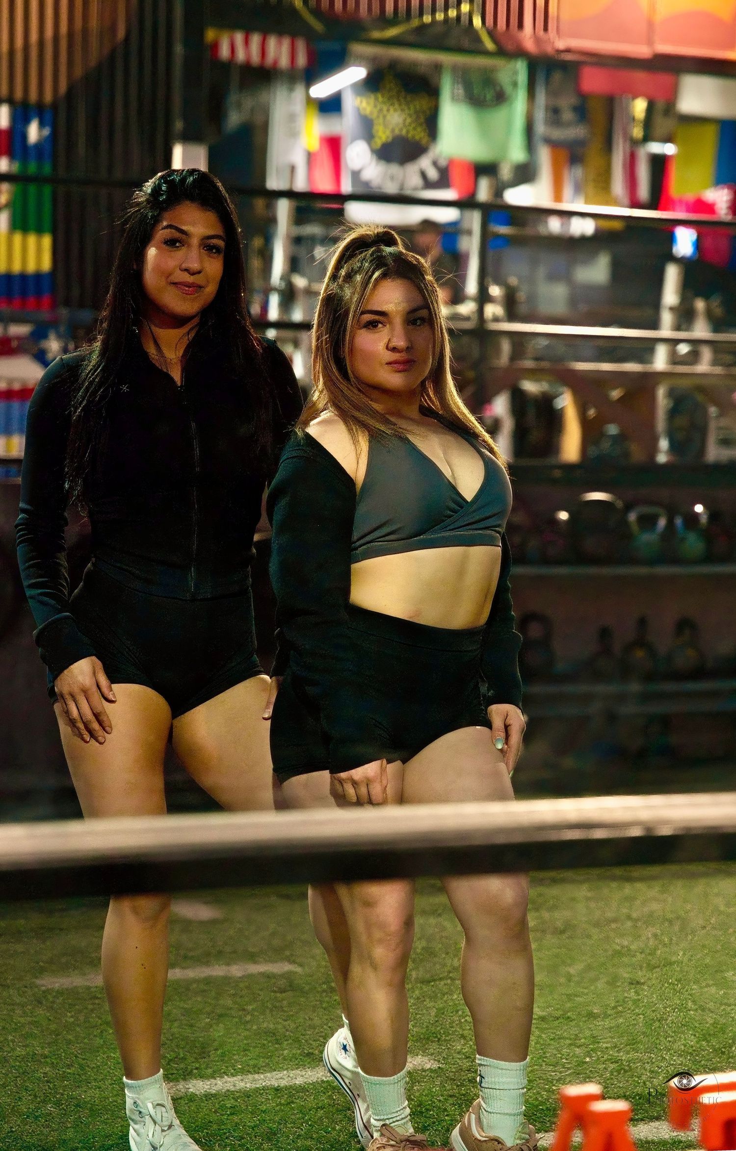 Two women standing confidently in a gym wearing workout attire during a fitness training session.