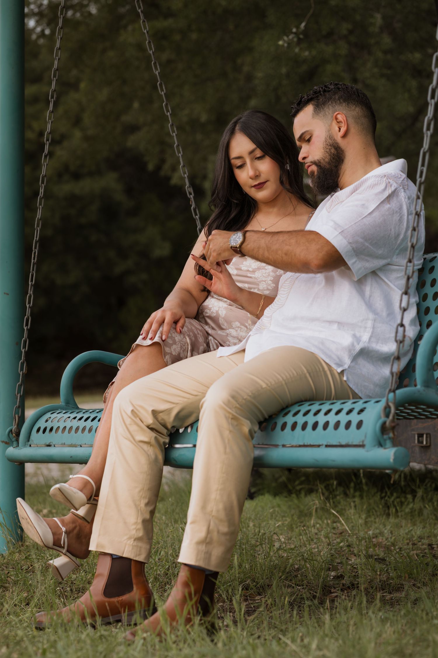Couple sitting closely on a teal porch swing, sharing an intimate moment outdoors surrounded by lush greenery.