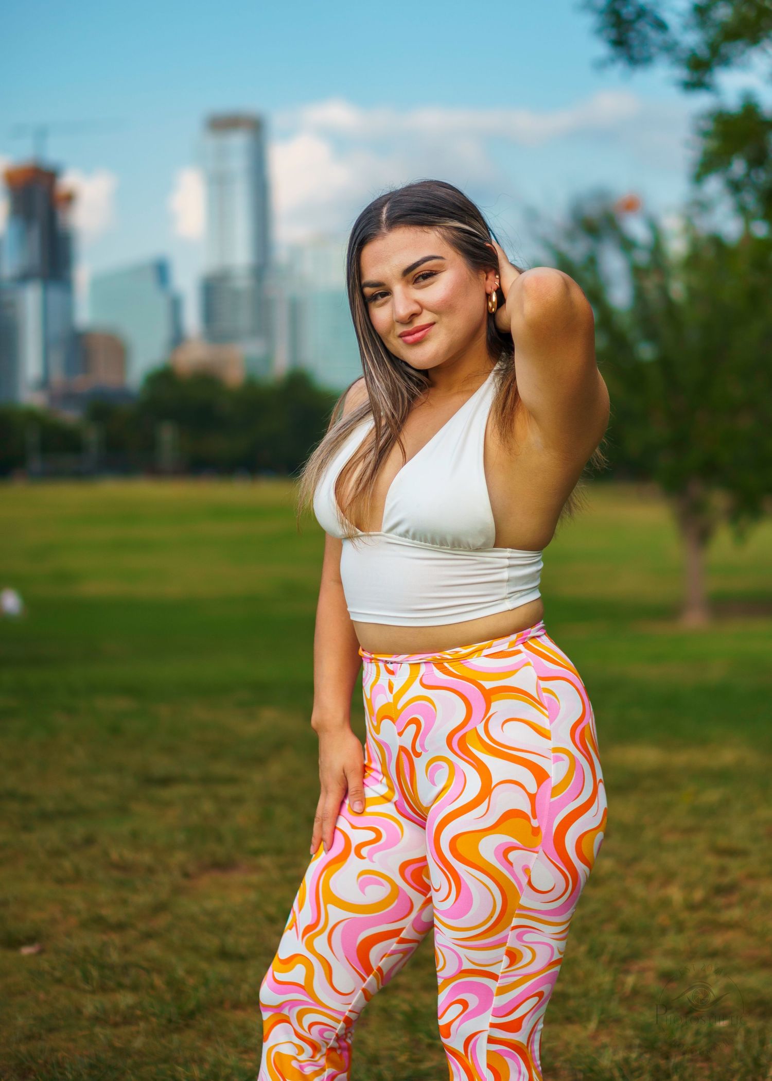 Woman posing outdoors in a park wearing a white top and colorful patterned pants.