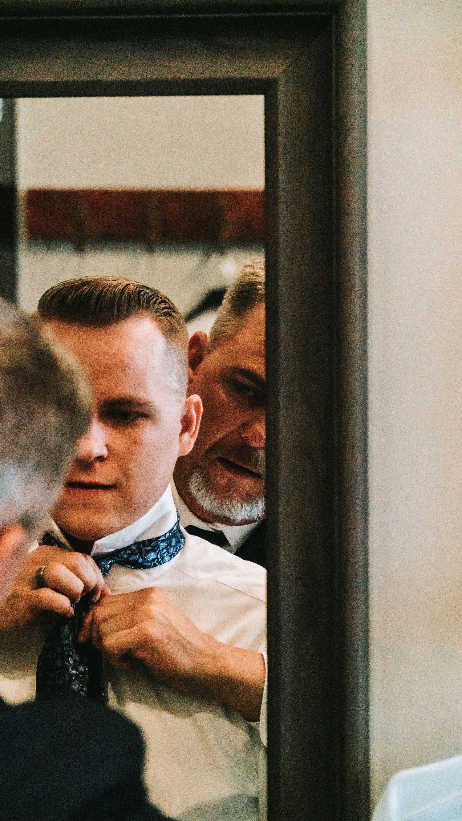 Groom adjusting his tie in front of a mirror while getting ready for his wedding.