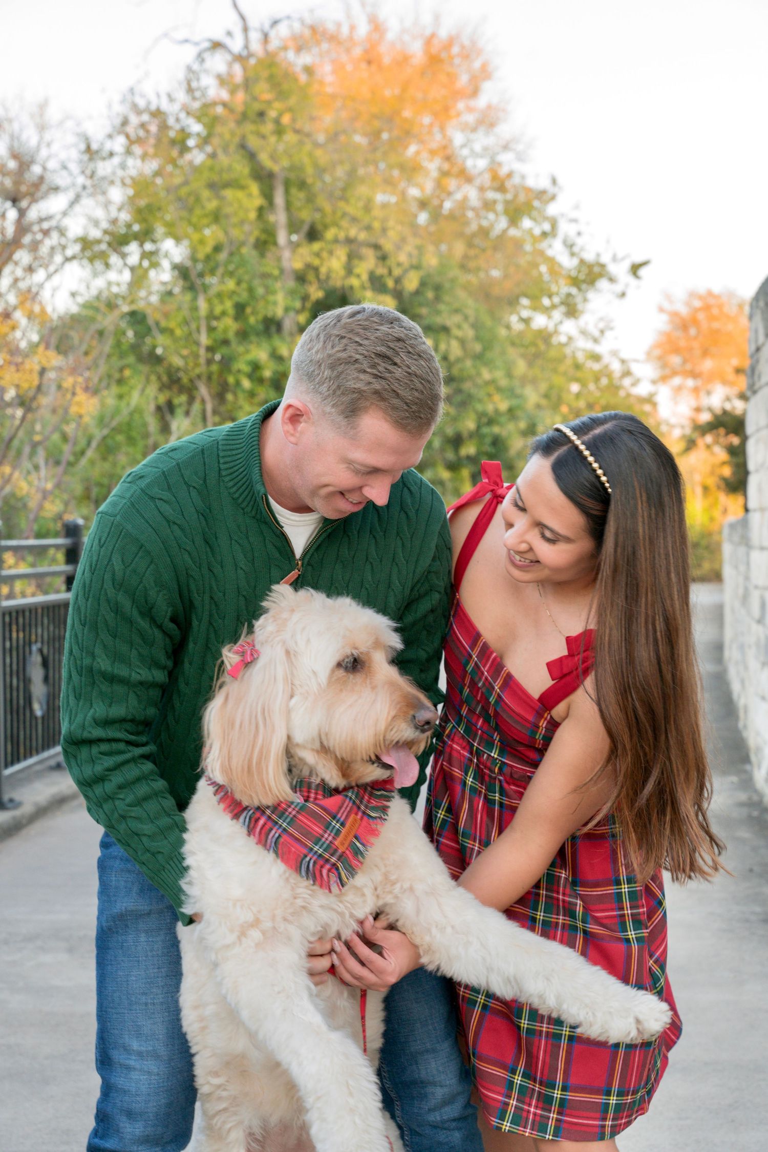 Couple standing outdoors in a park with their dog, posing together during a fall portrait session
