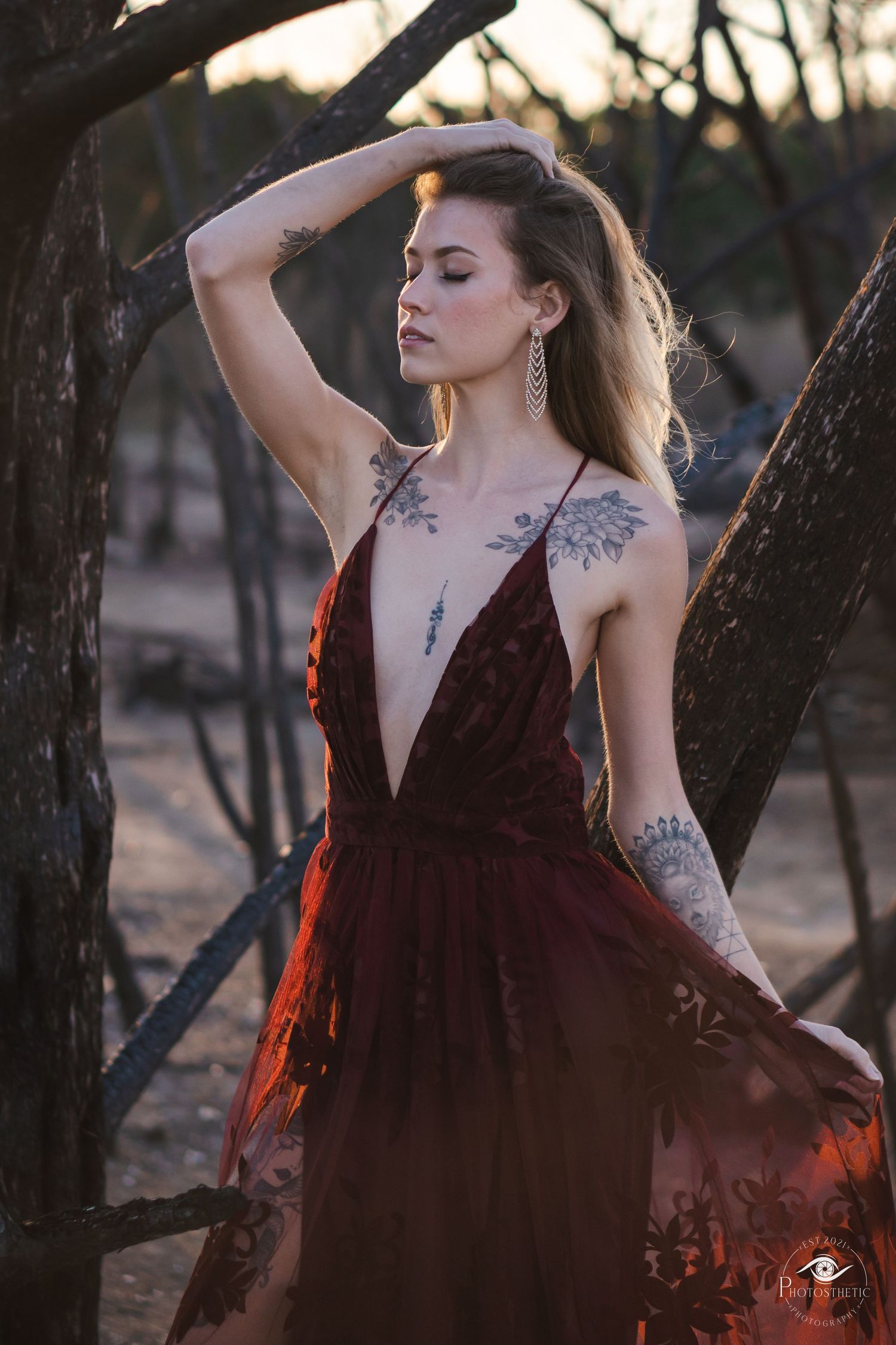 Artistic outdoor portrait of a tattooed woman in a flowing gown, captured in warm natural light.