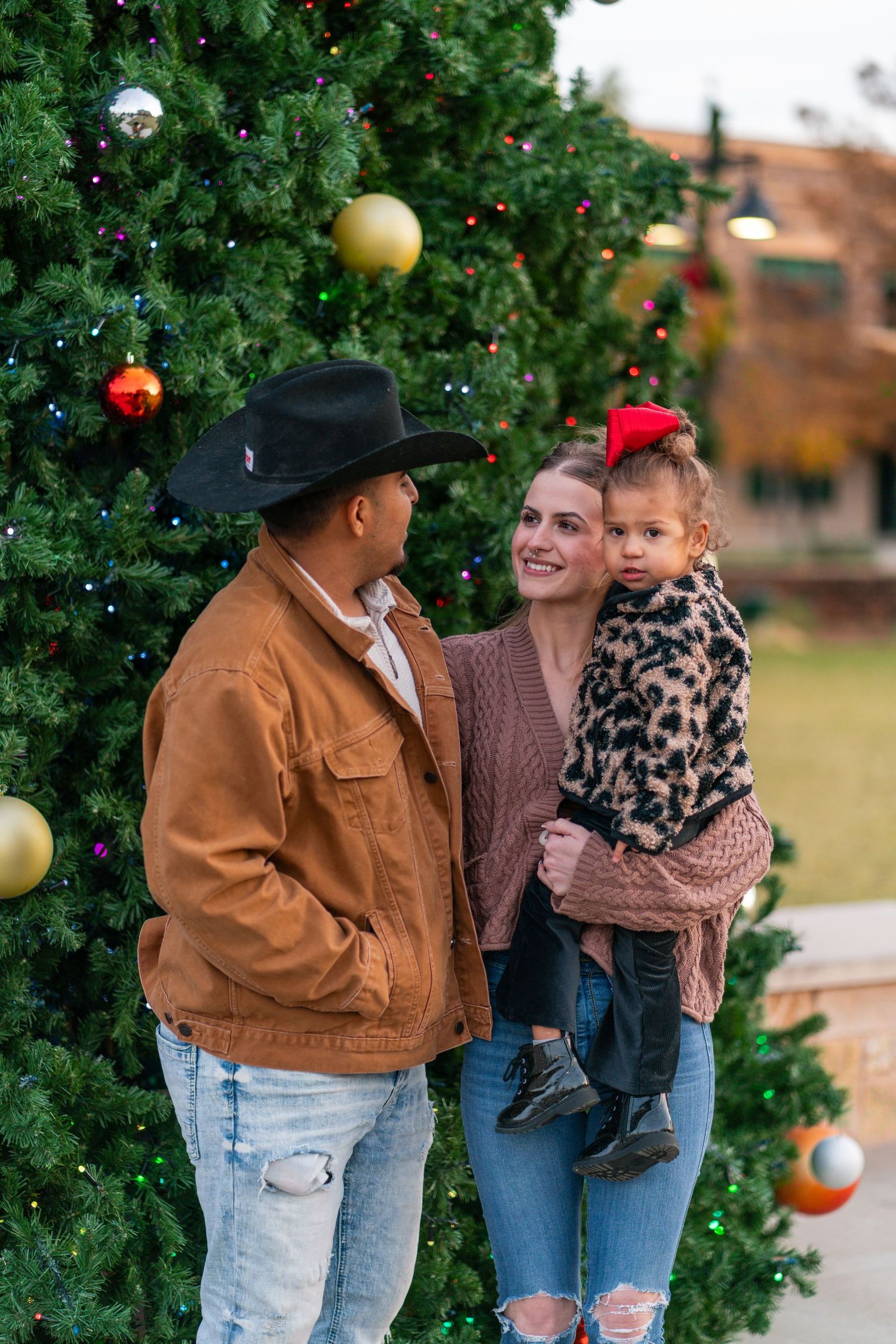 Family posing by decorated Christmas tree outdoors in casual winter attire at Santa Fe Plaza, 301 W Avenue A, Temple, TX 76501.