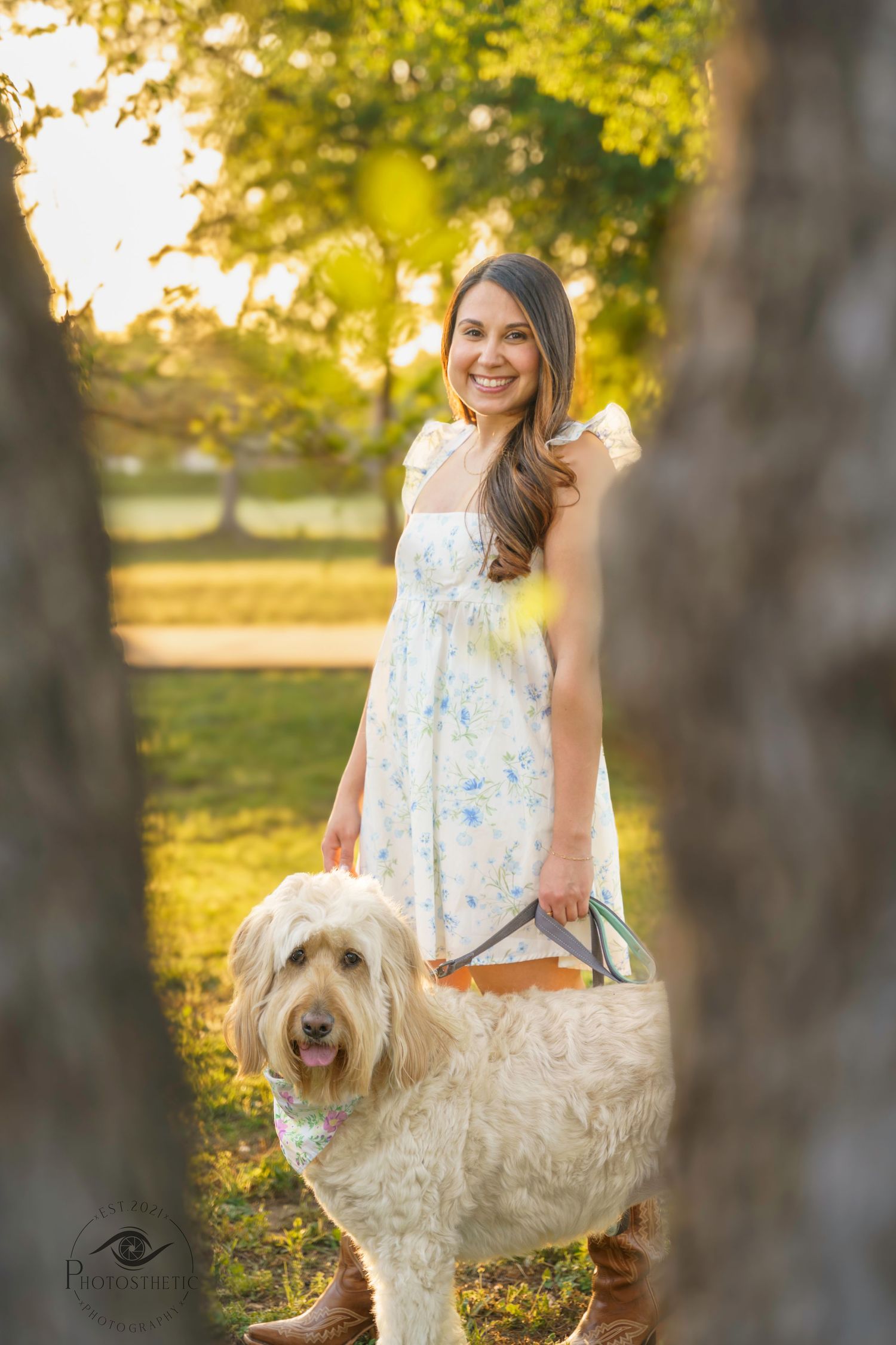 Woman standing outdoors in a park holding a large tote bag with her dog inside during golden hour.