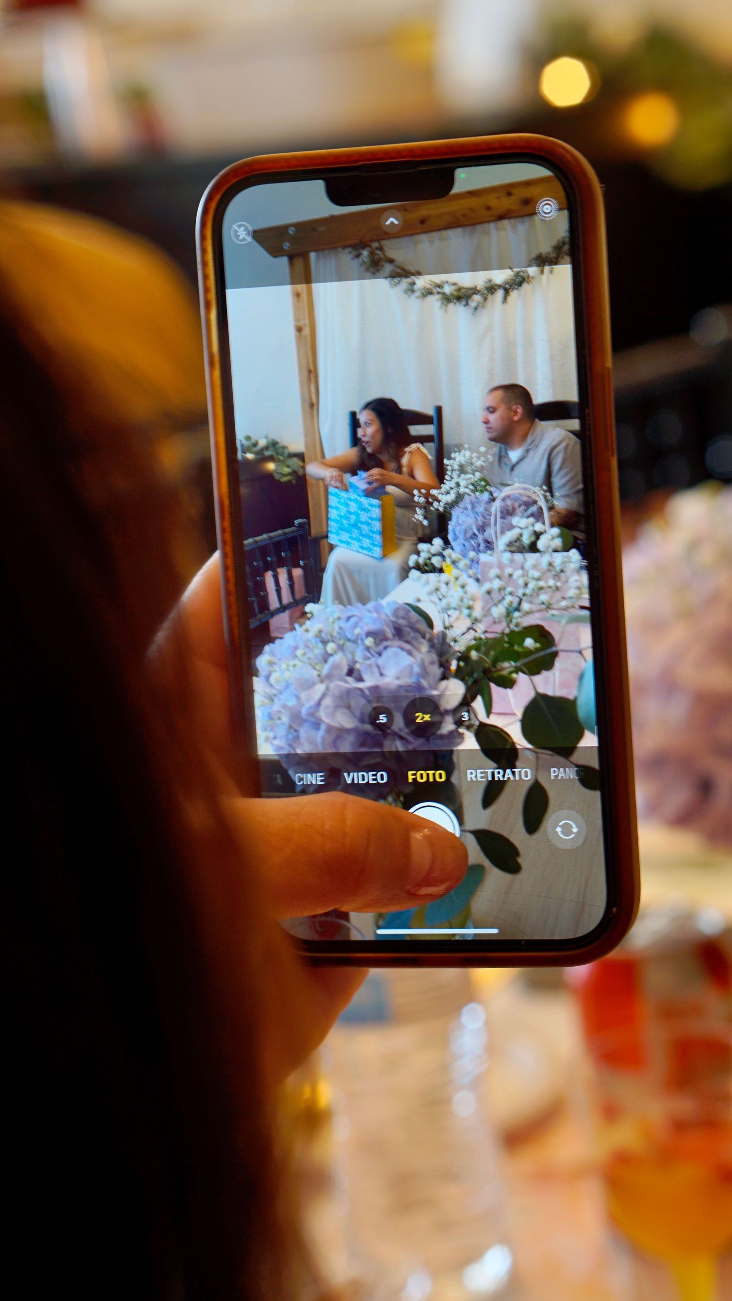 A phone screen displays a baby shower scene with decorative garlands and flowers in the foreground.