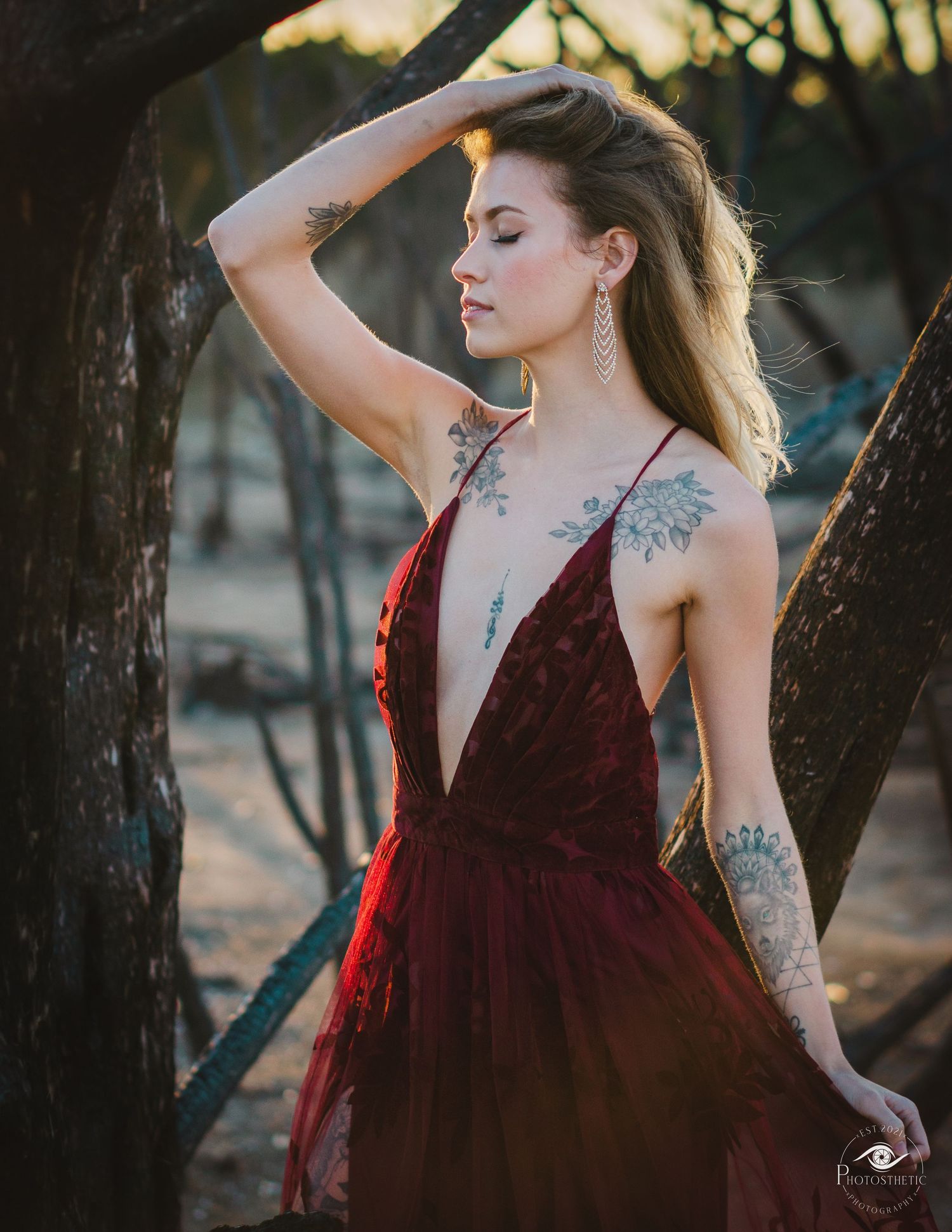Artistic outdoor portrait of a tattooed woman in a flowing gown, captured in warm natural light.