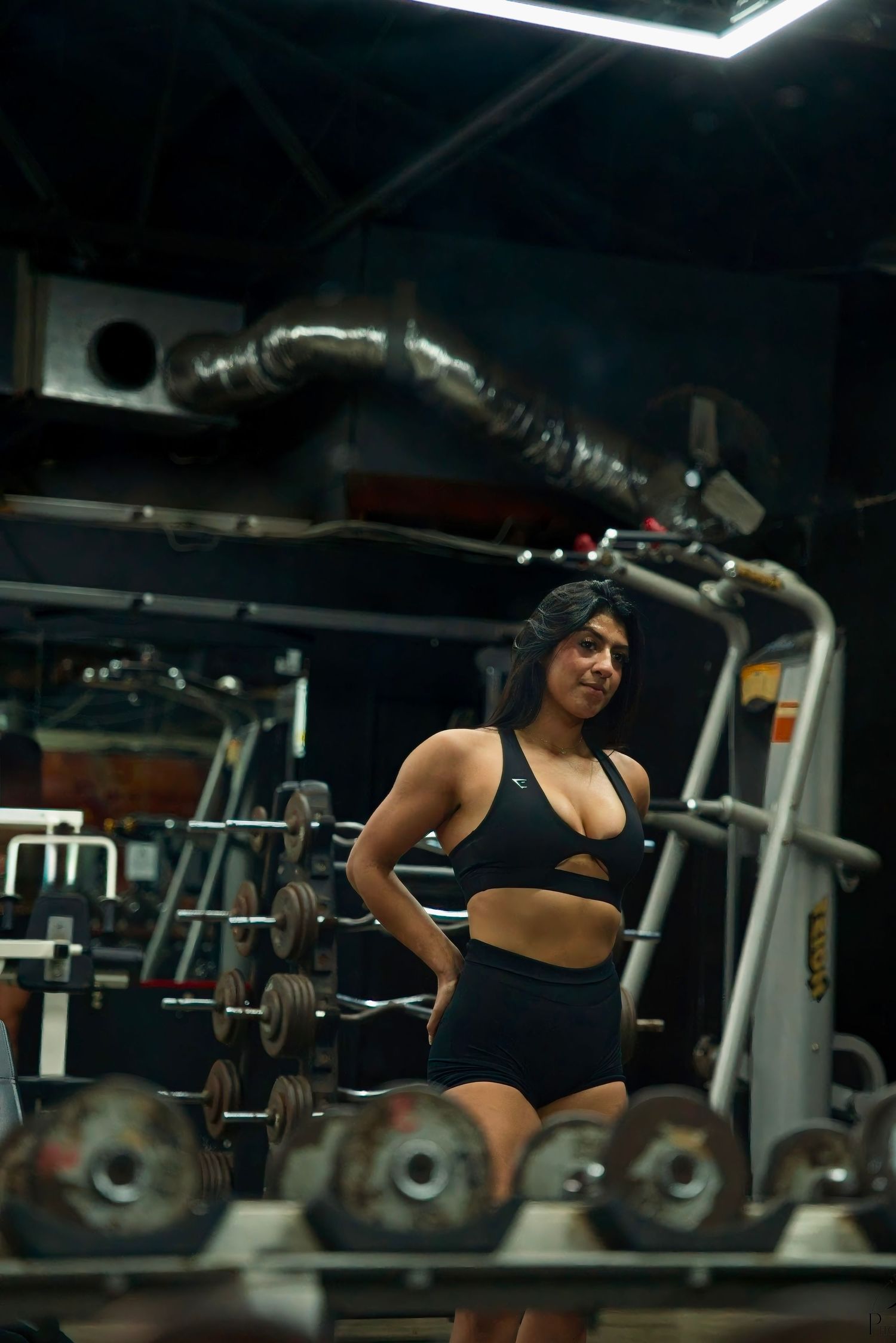 Female personal trainer standing confidently in a gym after strength training, with weightlifting equipment in the background.
