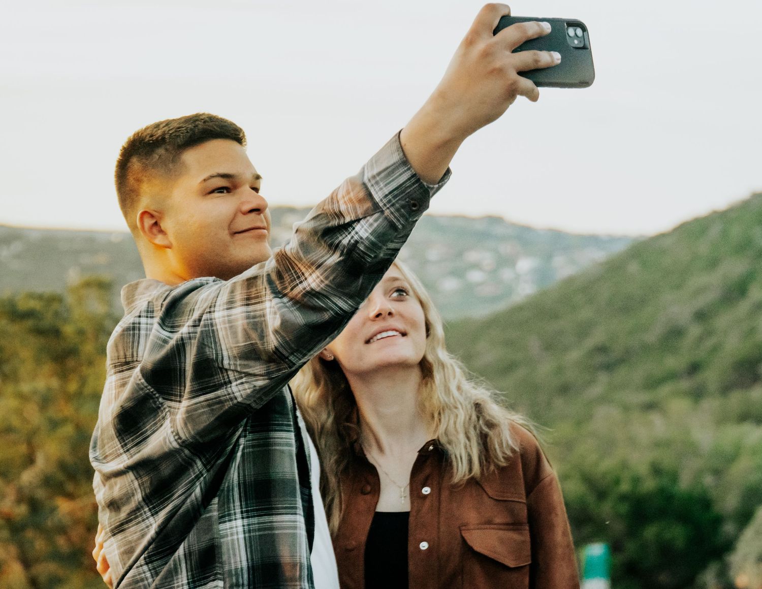 Couple taking selfies together in a scenic mountain setting at sunset.