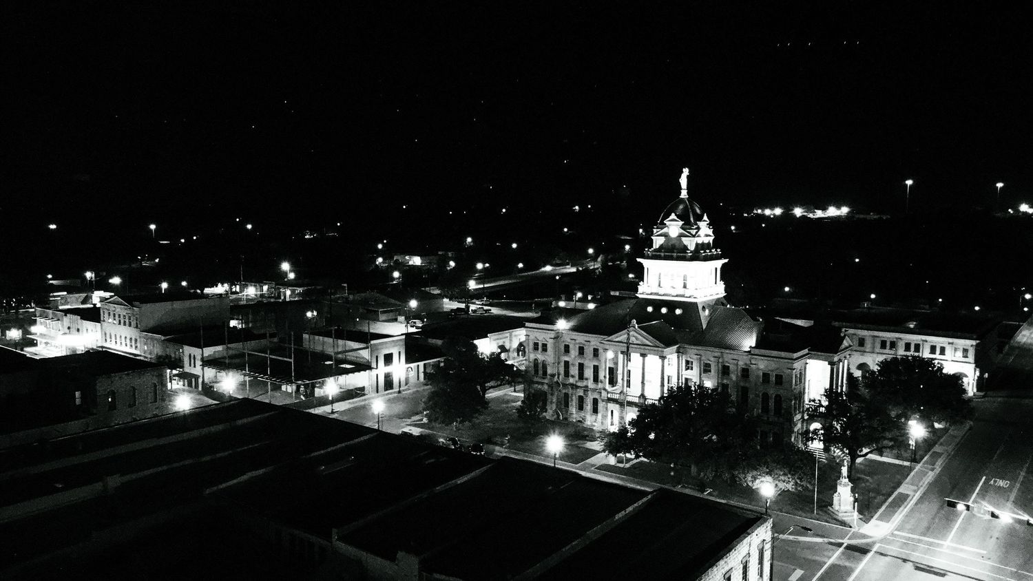 Black and white aerial view of a small city at night with illuminated buildings and streets.