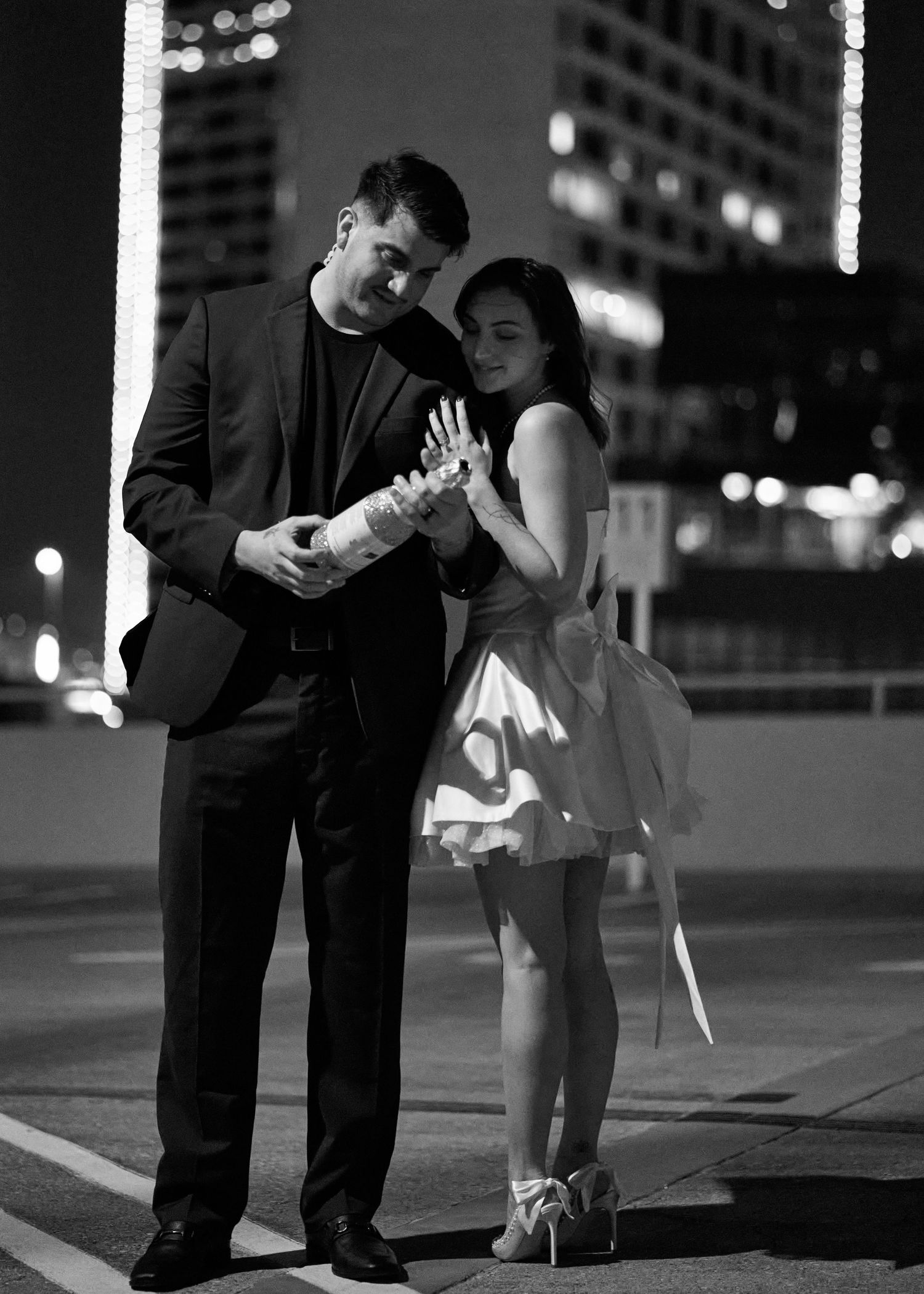 Couple in formal attire dance playfully on urban street at night.