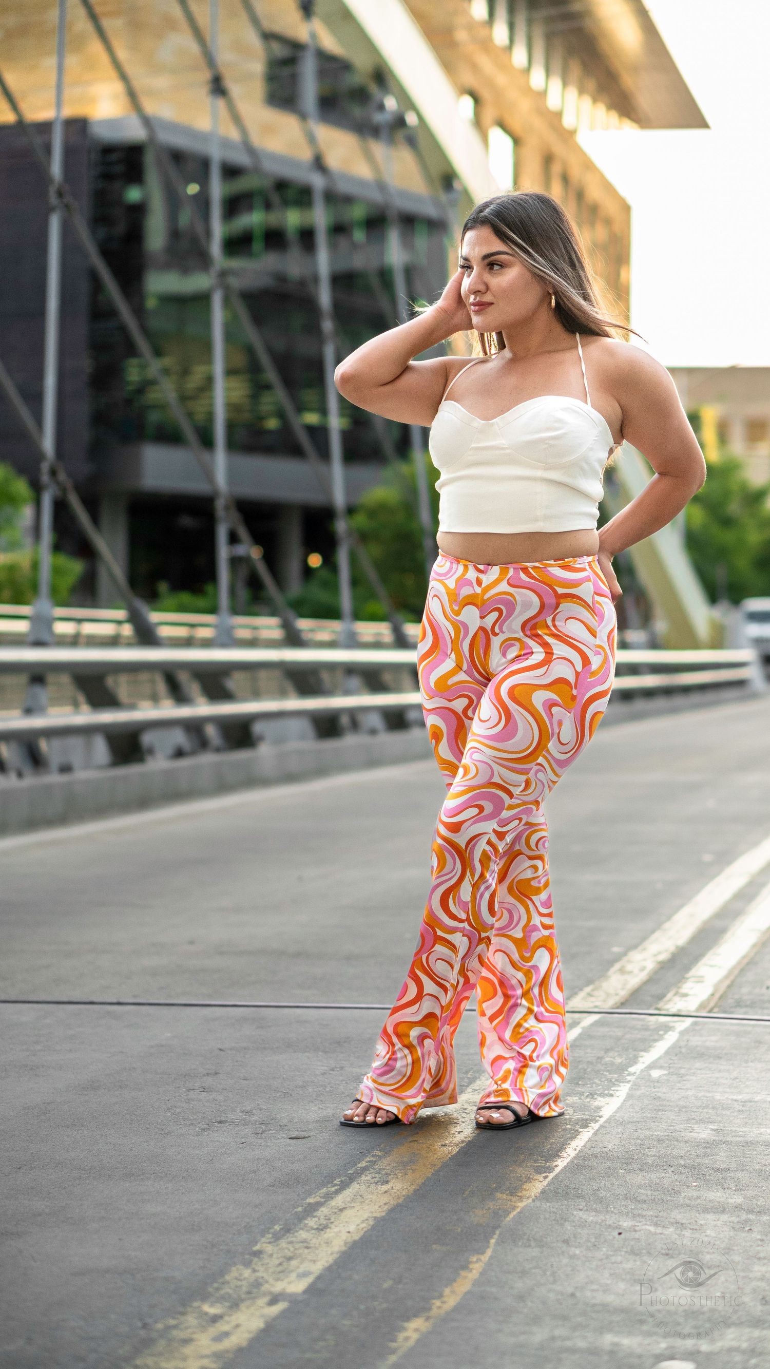 Woman walking confidently along a city street wearing patterned pants and a sleeveless top.