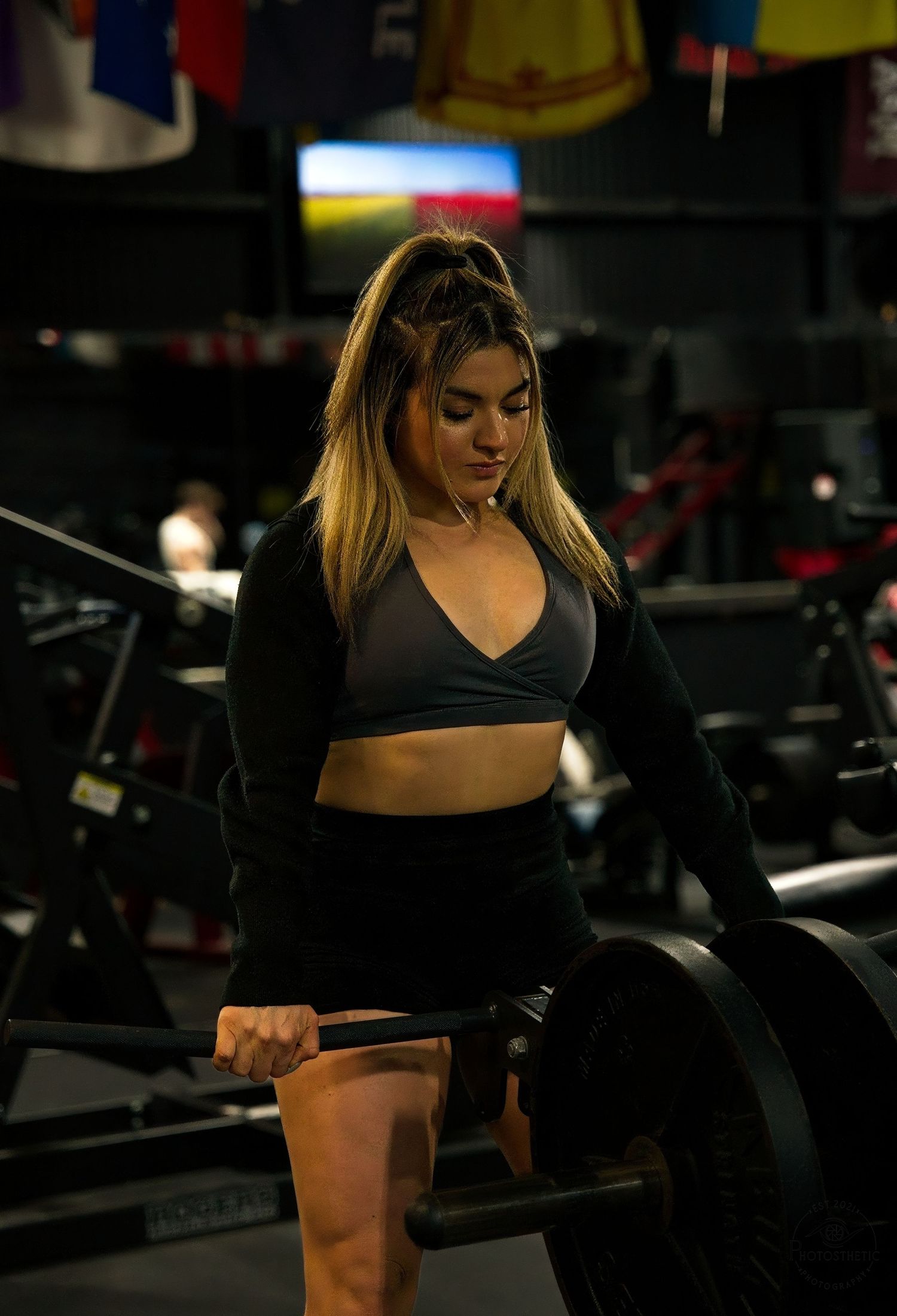 Female personal trainer performing a barbell deadlift in a gym, demonstrating proper strength training technique.