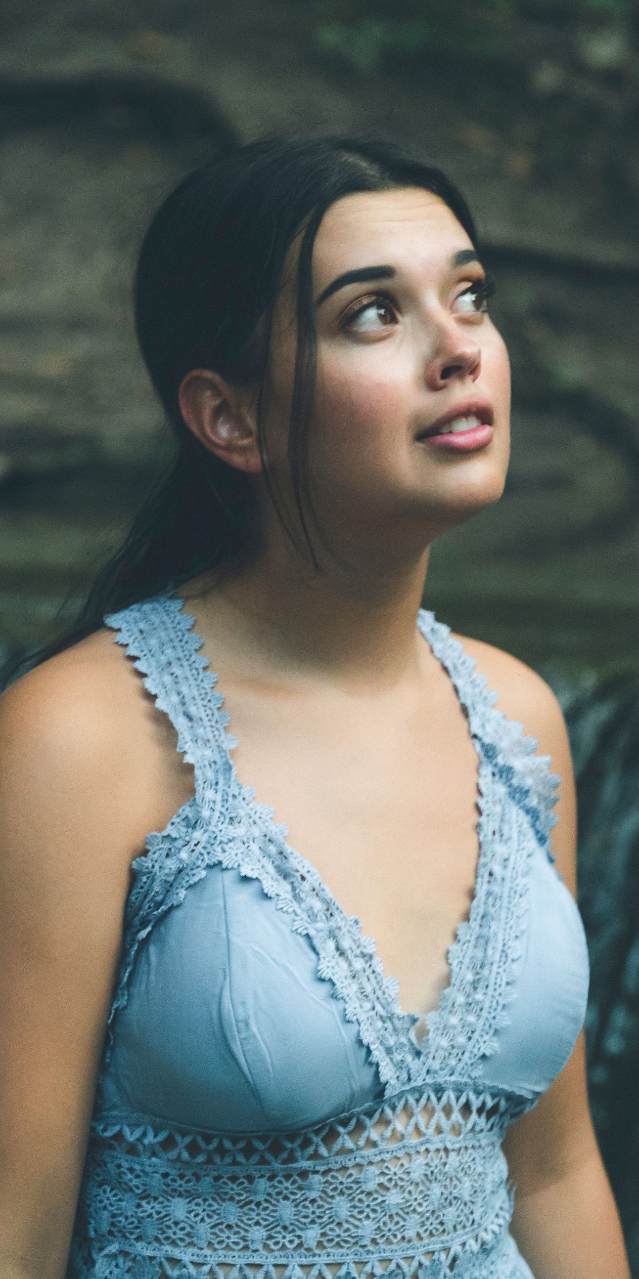 Outdoor portrait of a woman wearing a light blue dress, looking upward while standing near a rock wall