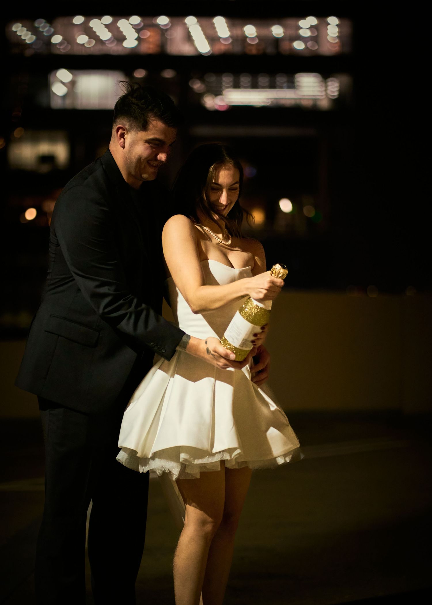 A couple in formal attire dance together under dim lighting at an evening event.