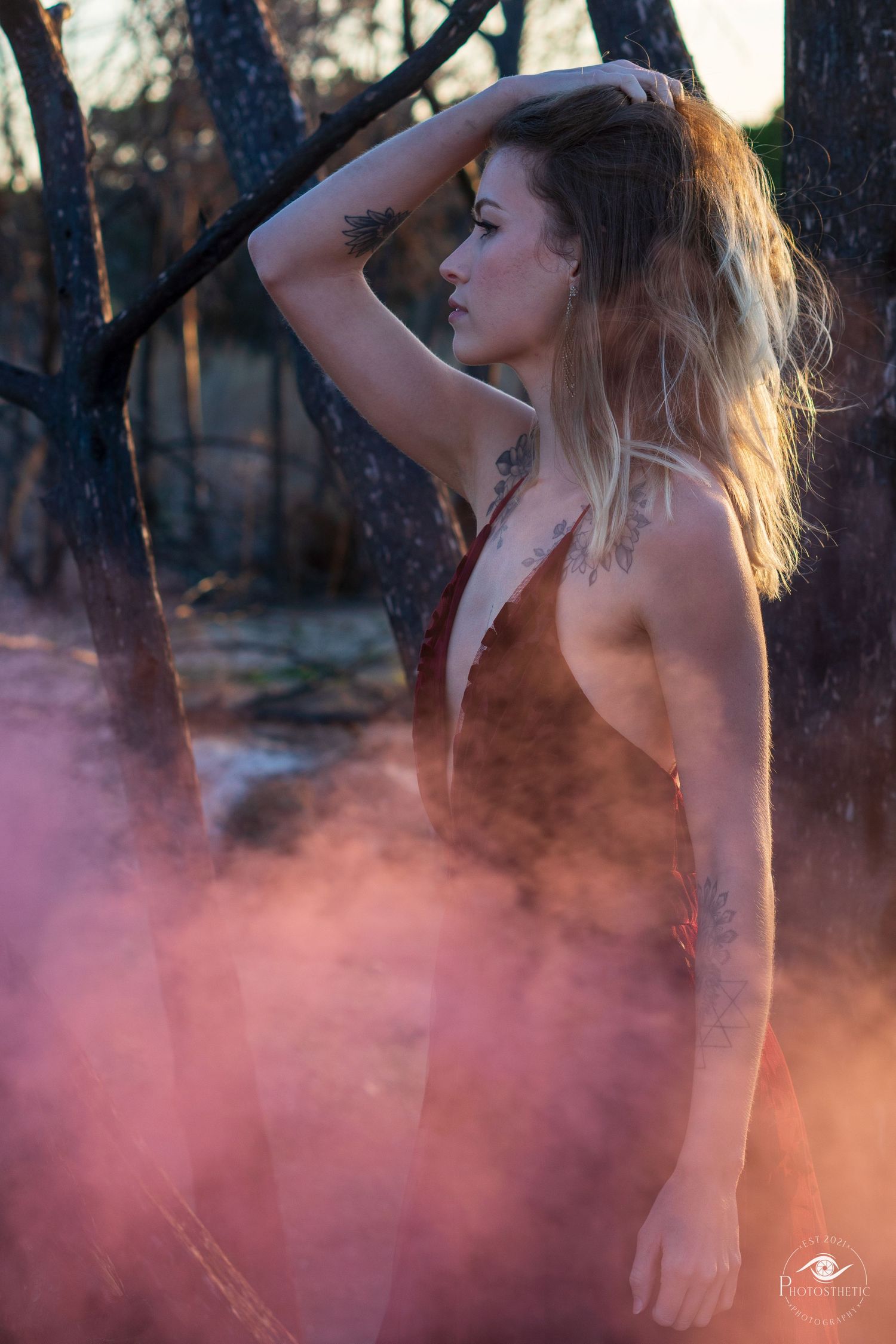 Artistic outdoor portrait of a tattooed woman in a flowing gown, captured in warm natural light.