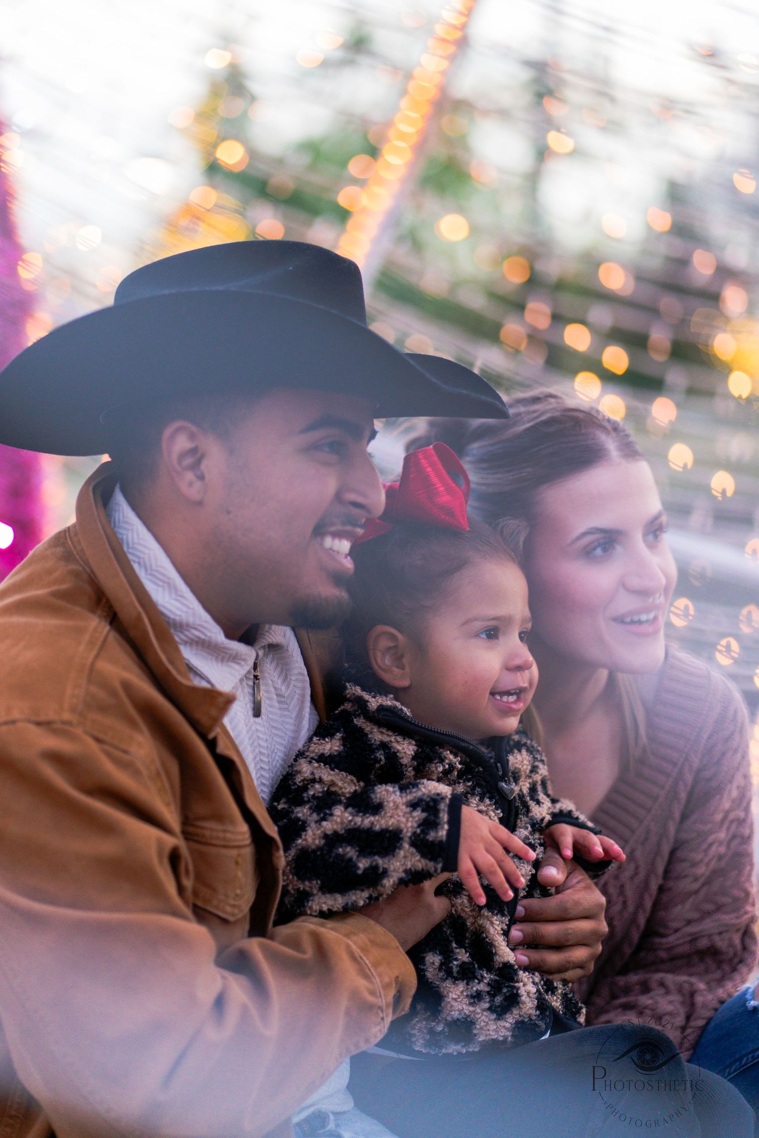 Family sitting together outdoors with holiday lights, smiling and sharing a joyful moment during a winter portrait session.