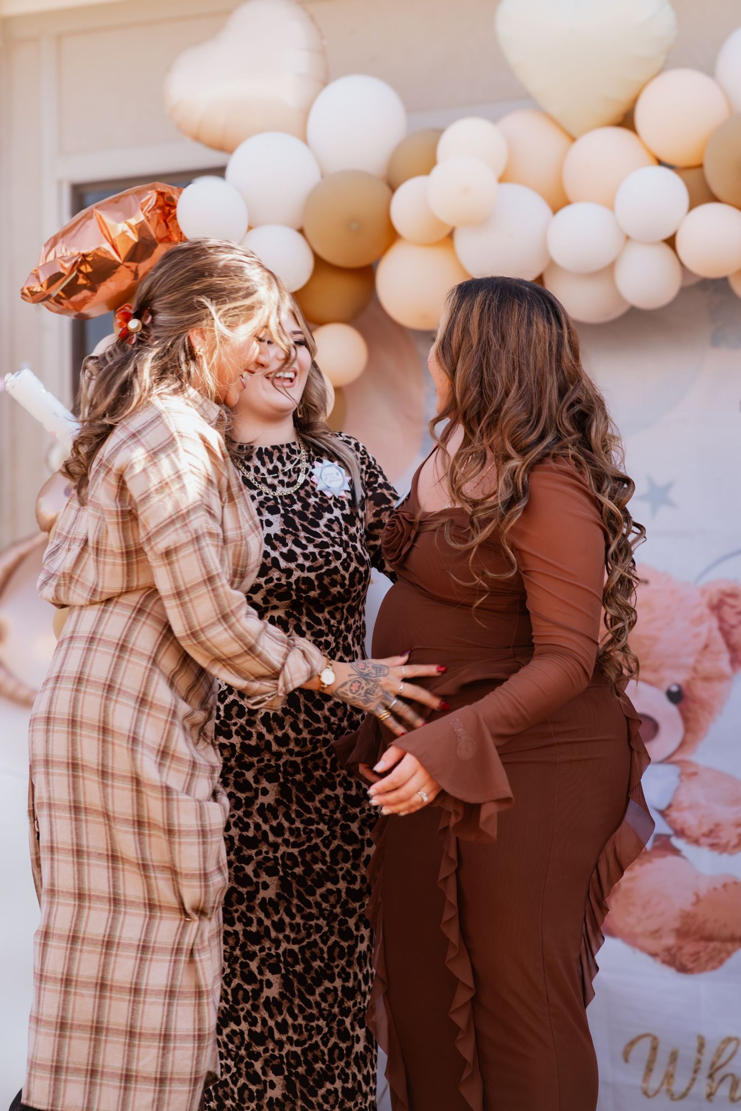 Three people sharing joyful moments and embracing at a celebration decorated with white balloons.