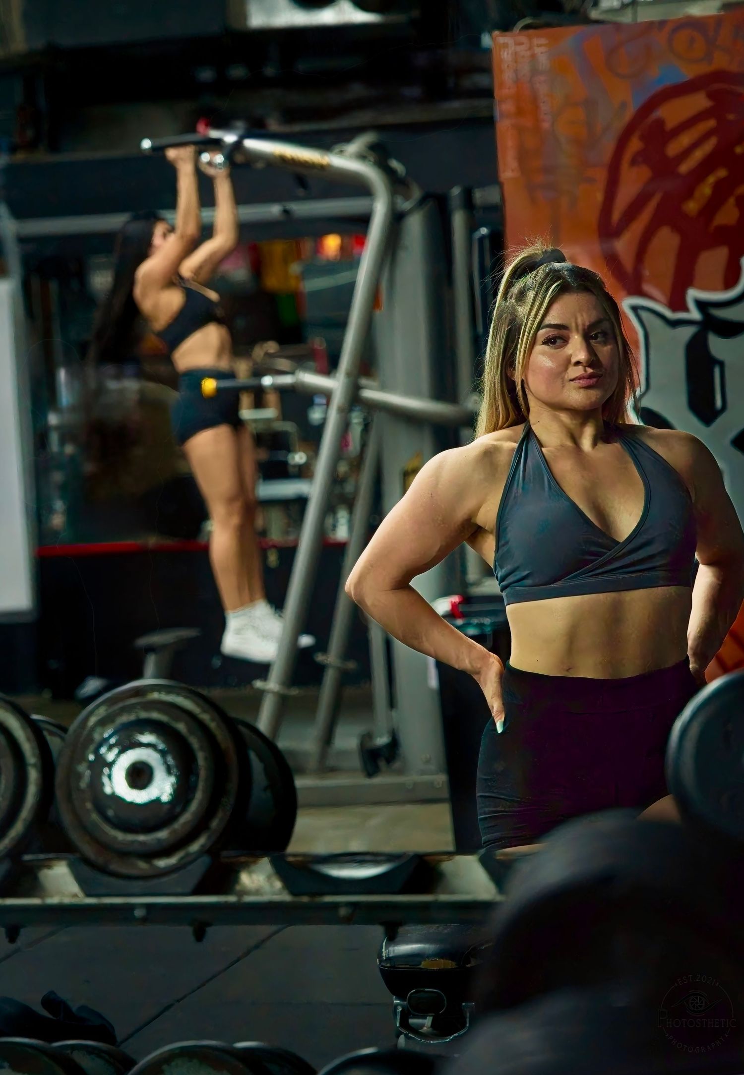 Female personal trainer standing confidently in a gym after strength training, with weightlifting equipment in the background.