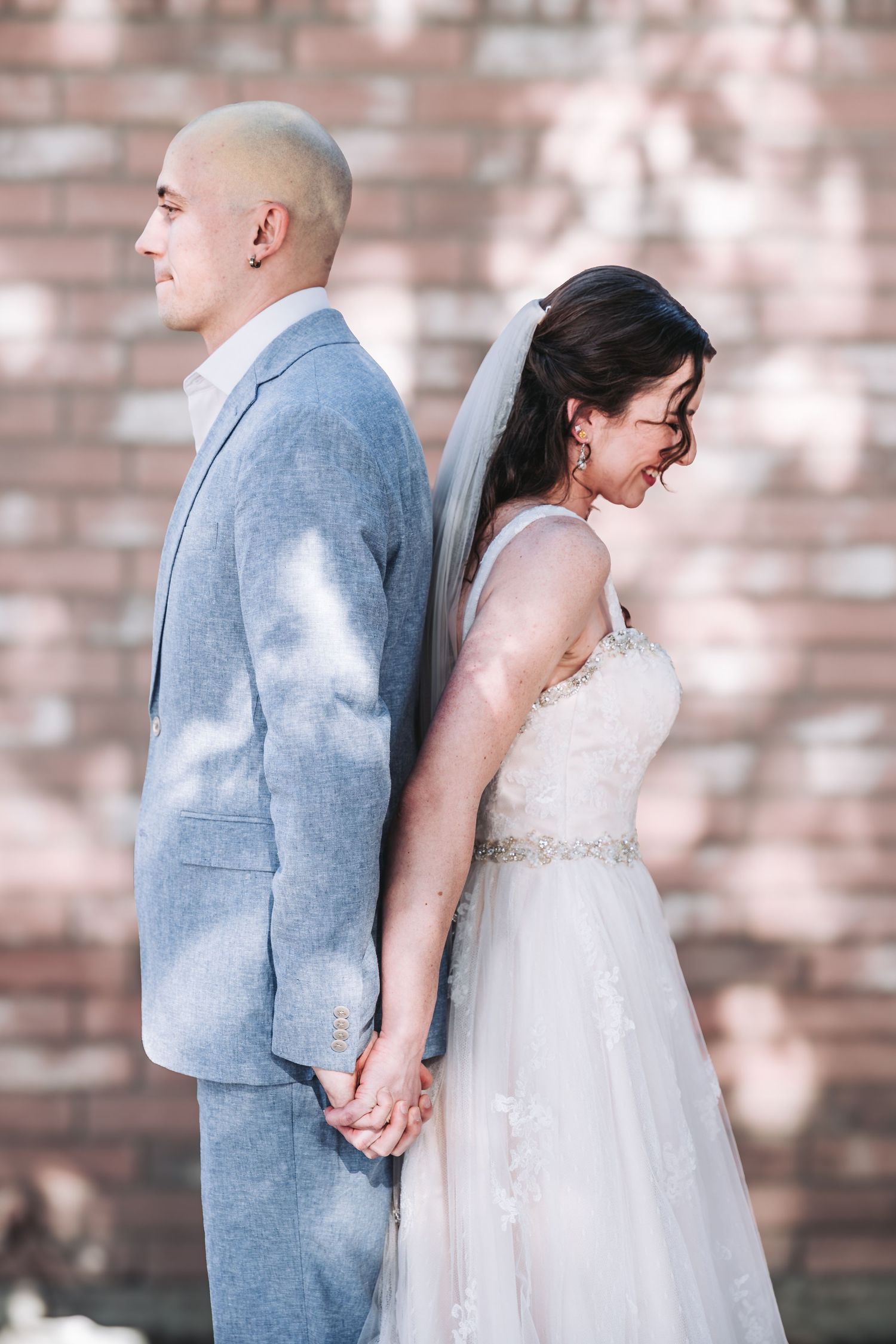 Bride and groom standing back to back holding hands during an outdoor wedding moment.