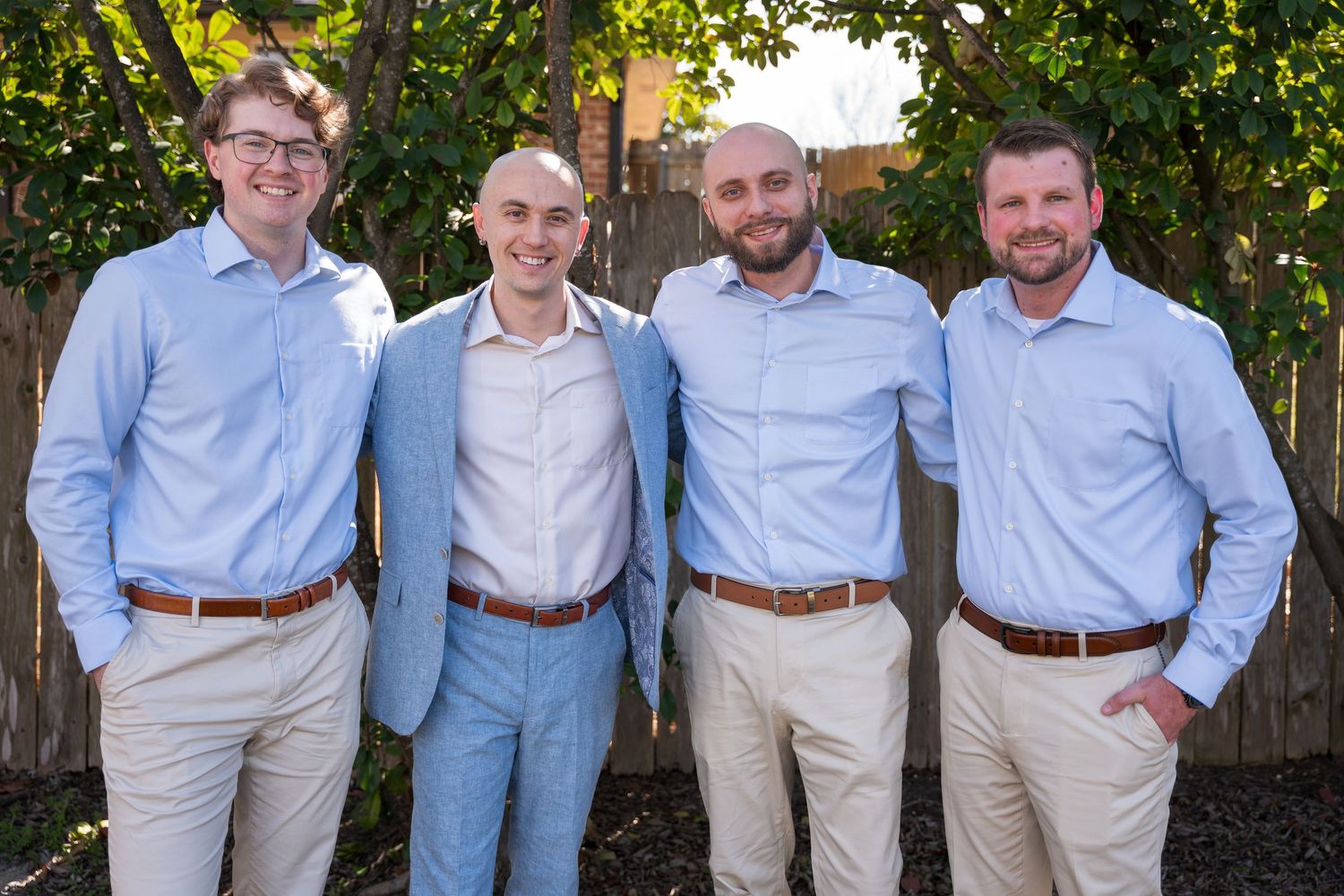Groomsmen in light blue shirts and khaki pants pose casually outdoors.