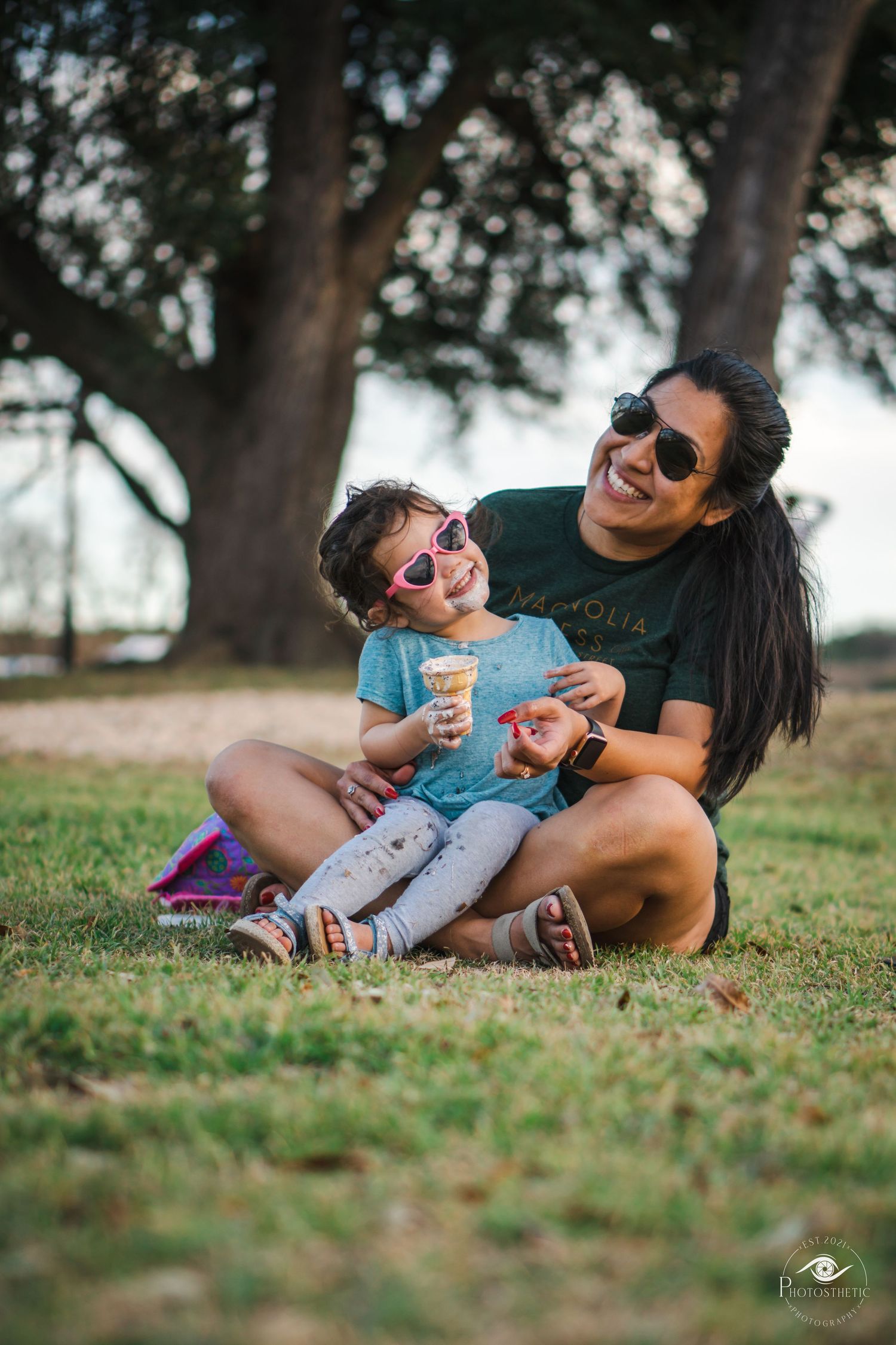 Mother sitting on grass with her young child, laughing together during an outdoor lifestyle portrait.