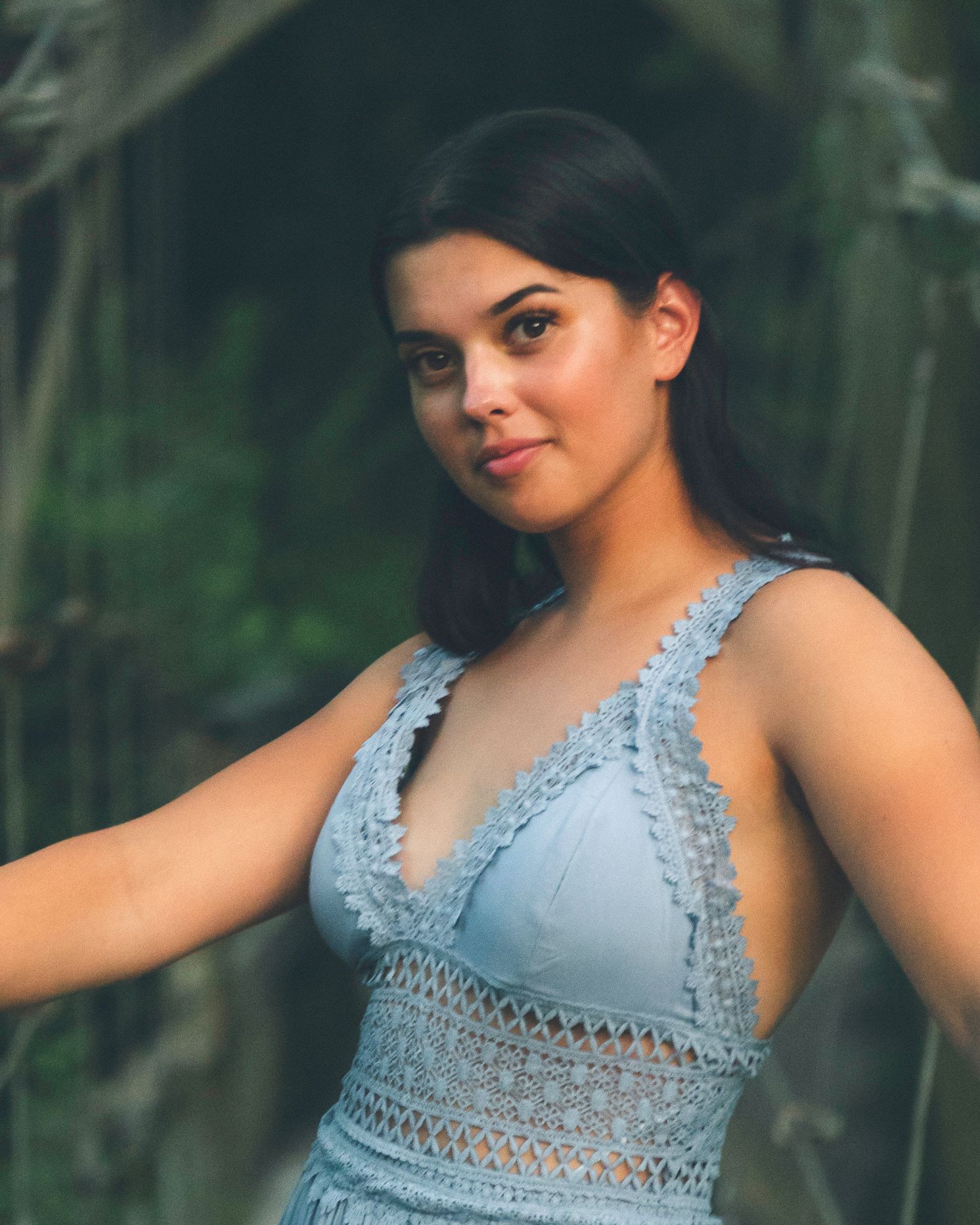 Outdoor portrait of a woman wearing a blue lace dress standing near a creek in natural light.