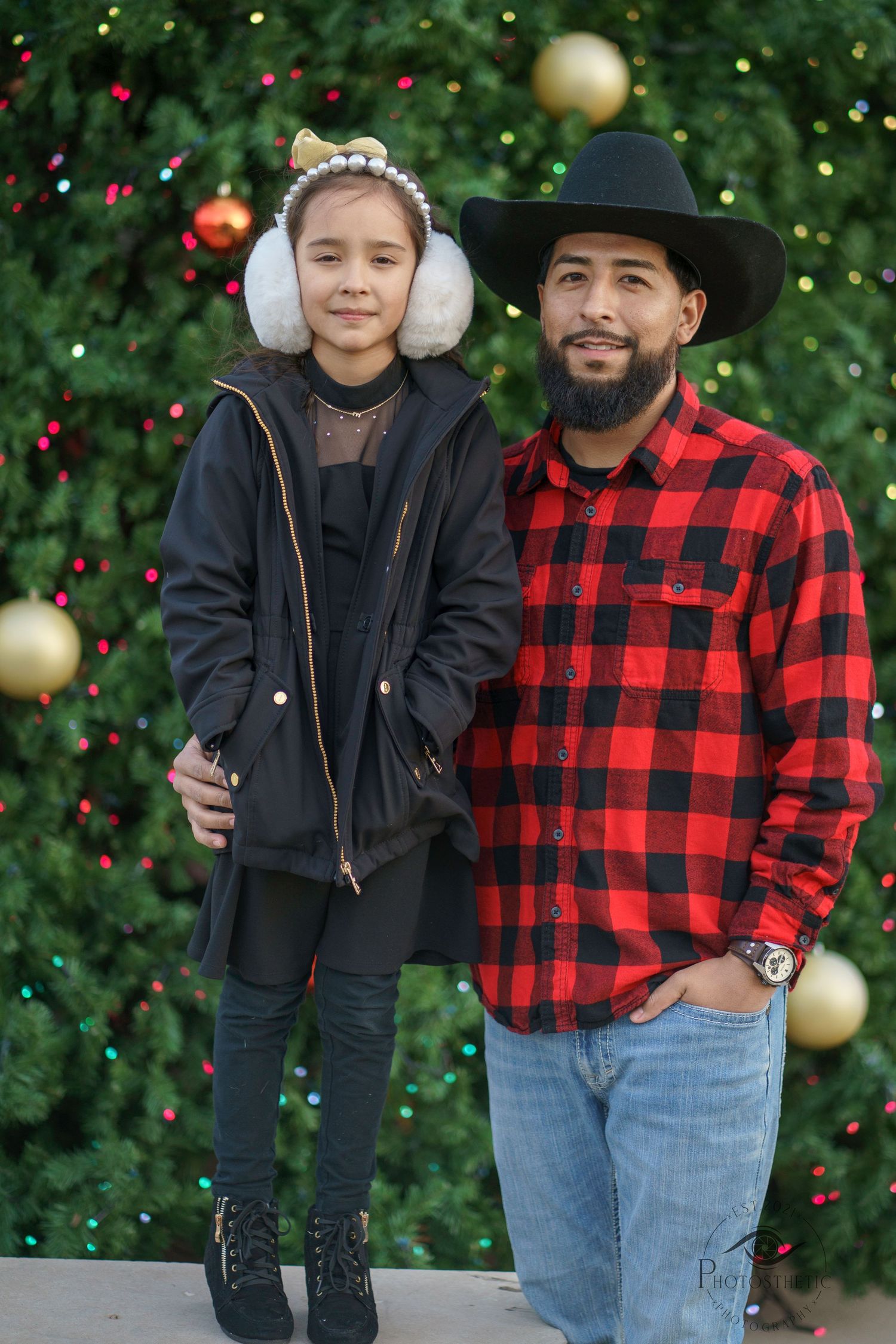 Festive holiday portrait of a father and daughter standing together outdoors with Christmas decorations.