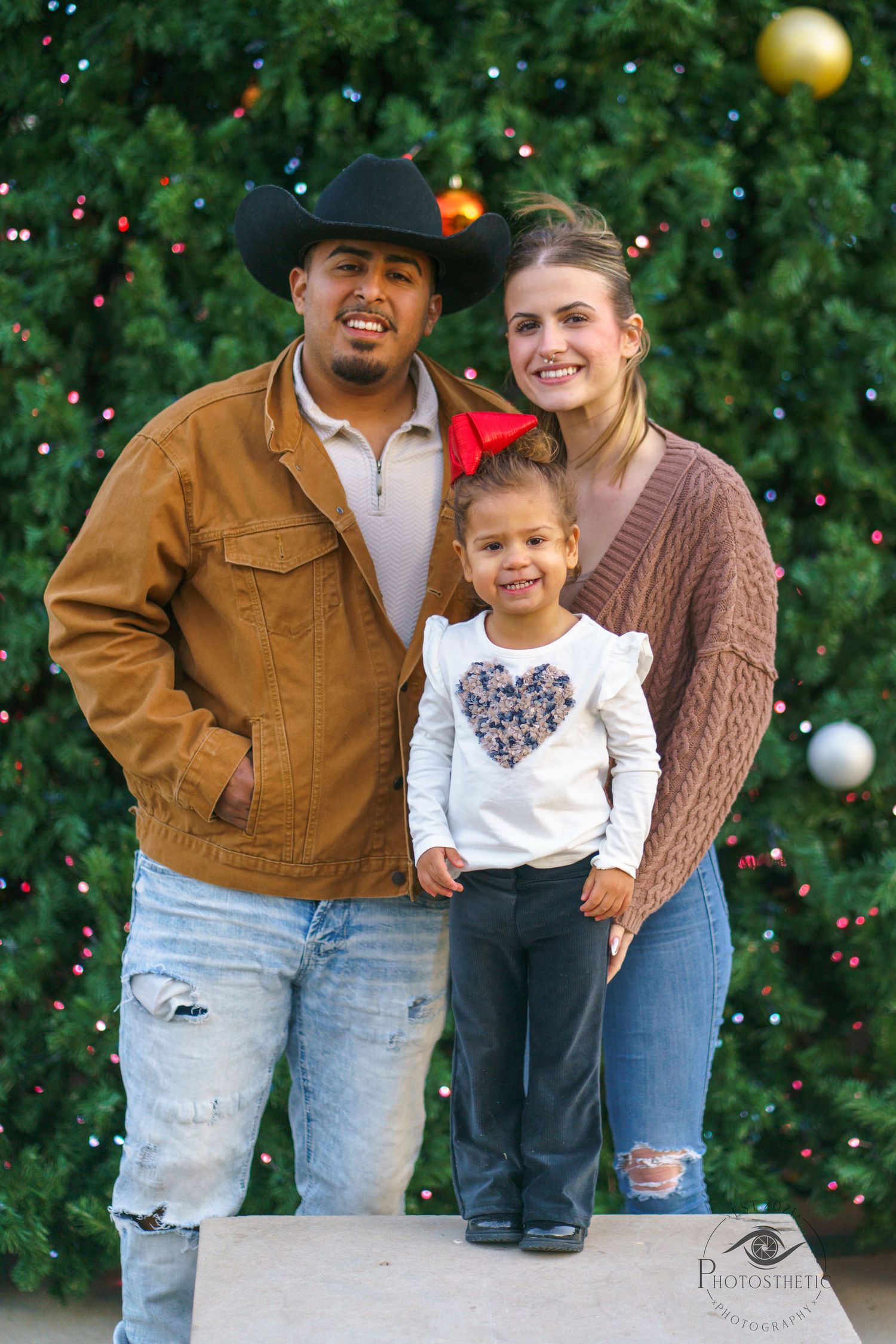 Family standing together outdoors with holiday lights, smiling and sharing a joyful moment during a winter portrait session.