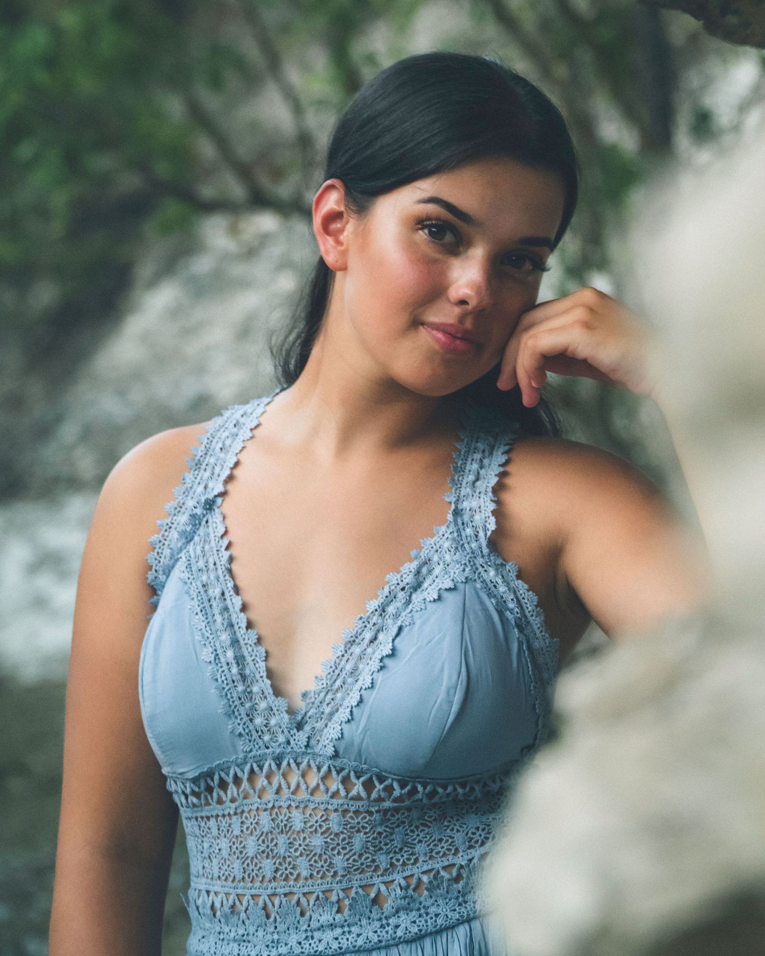 Close-up outdoor portrait of a woman wearing a blue dress near a creek with soft natural light.