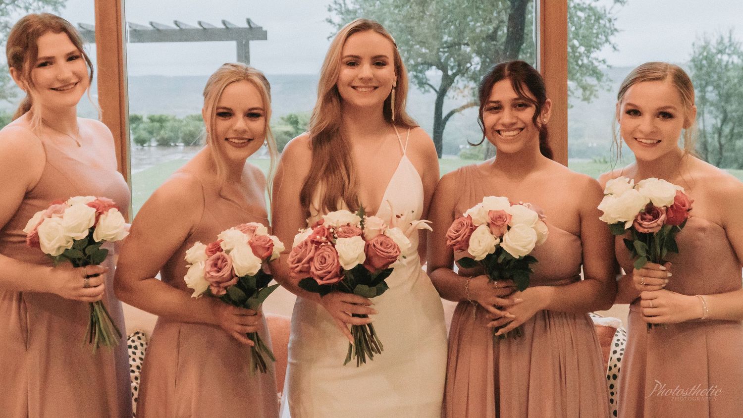 Bride standing with her bridesmaids holding floral bouquets during an indoor wedding portrait.