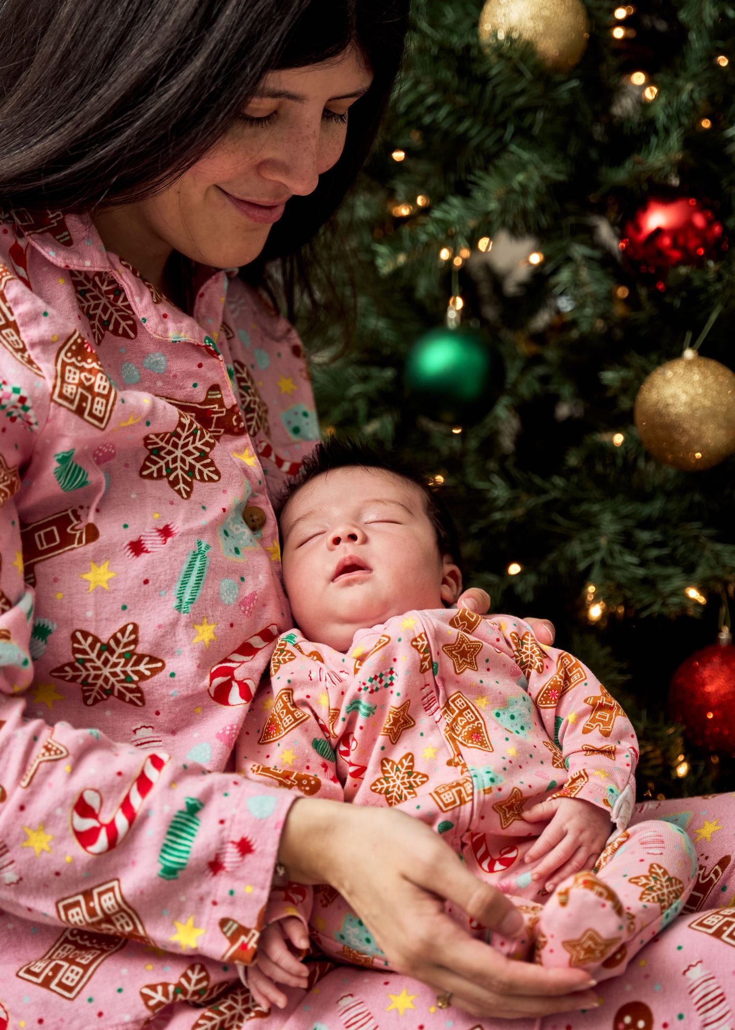 Mother and newborn in festive pajamas sleeping peacefully by Christmas tree lights during a Mommy n Me session in Temple, Texas.