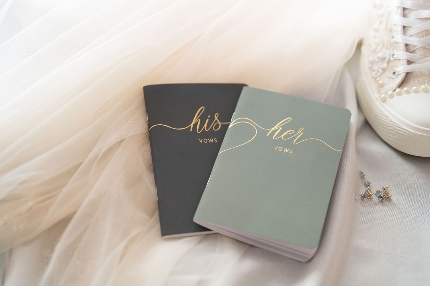 Elegant wedding vows and stationery in soft sage green and charcoal gray tones on white fabric background.