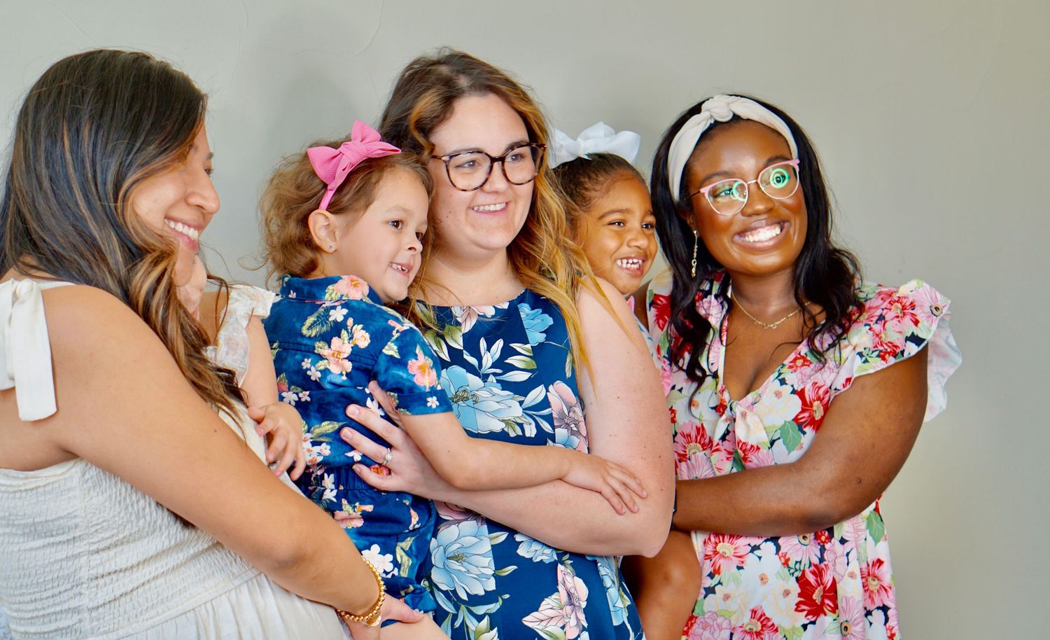 A group of friends in floral and blue dresses laugh together during a celebratory gathering.