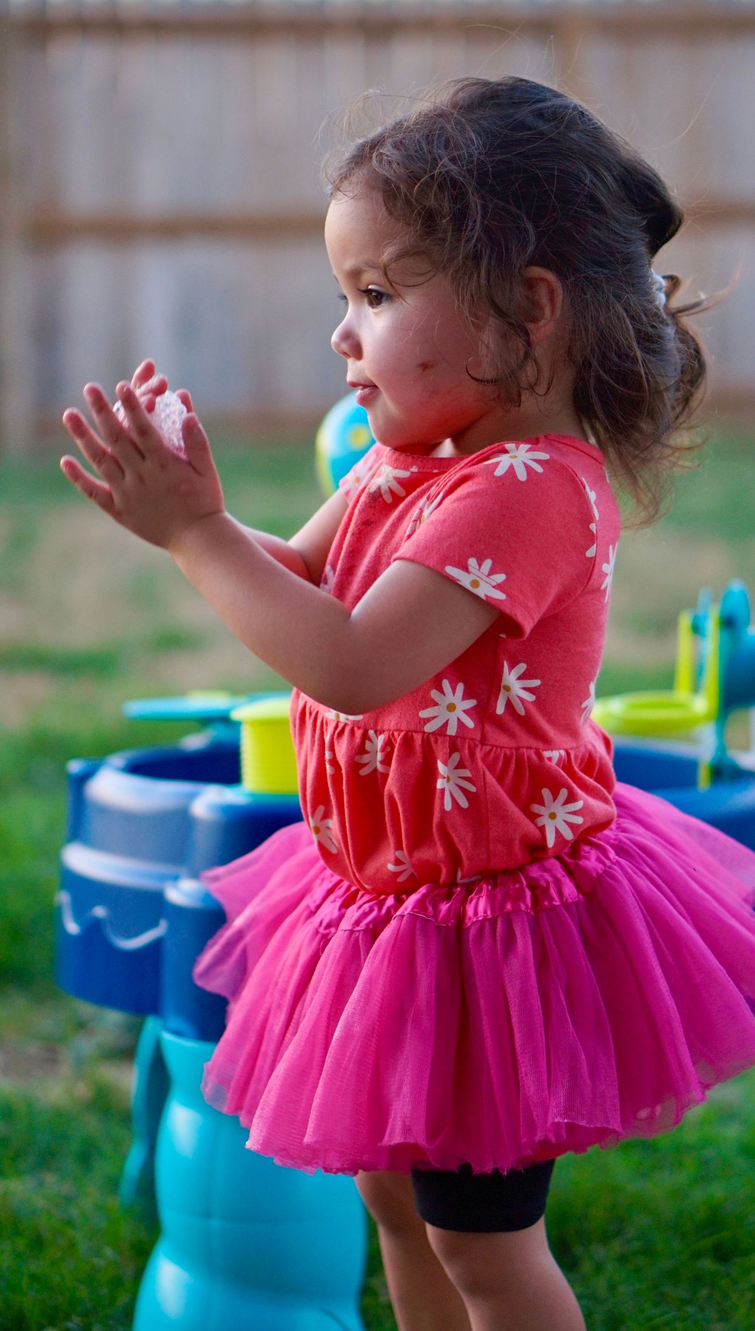 Young child in pink tutu dress plays outdoors with toys.