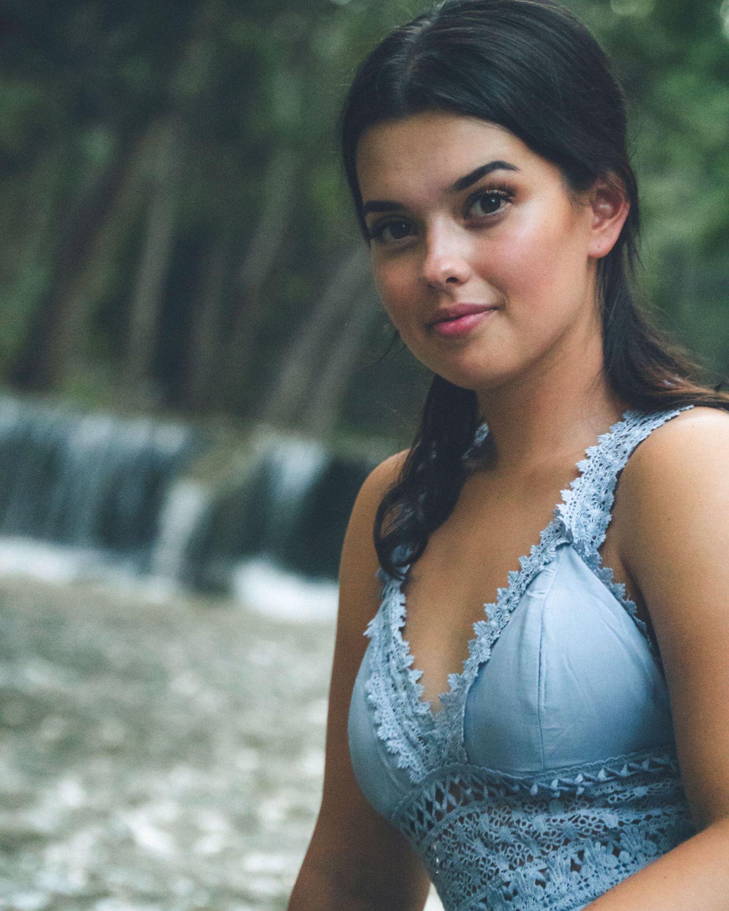 Outdoor portrait of a woman in a blue dress standing near a creek and small waterfall