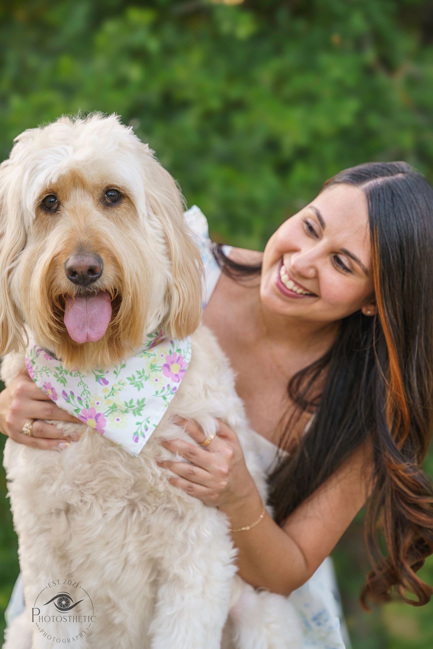 Woman smiling while holding her fluffy dog wearing a floral bandana during an outdoor portrait session.