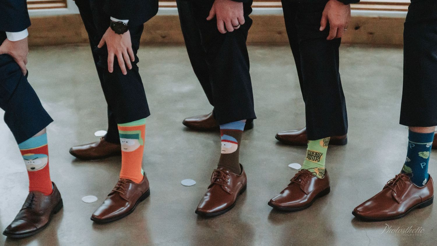 Groomsmen standing side by side showing colorful socks and dress shoes during a wedding.