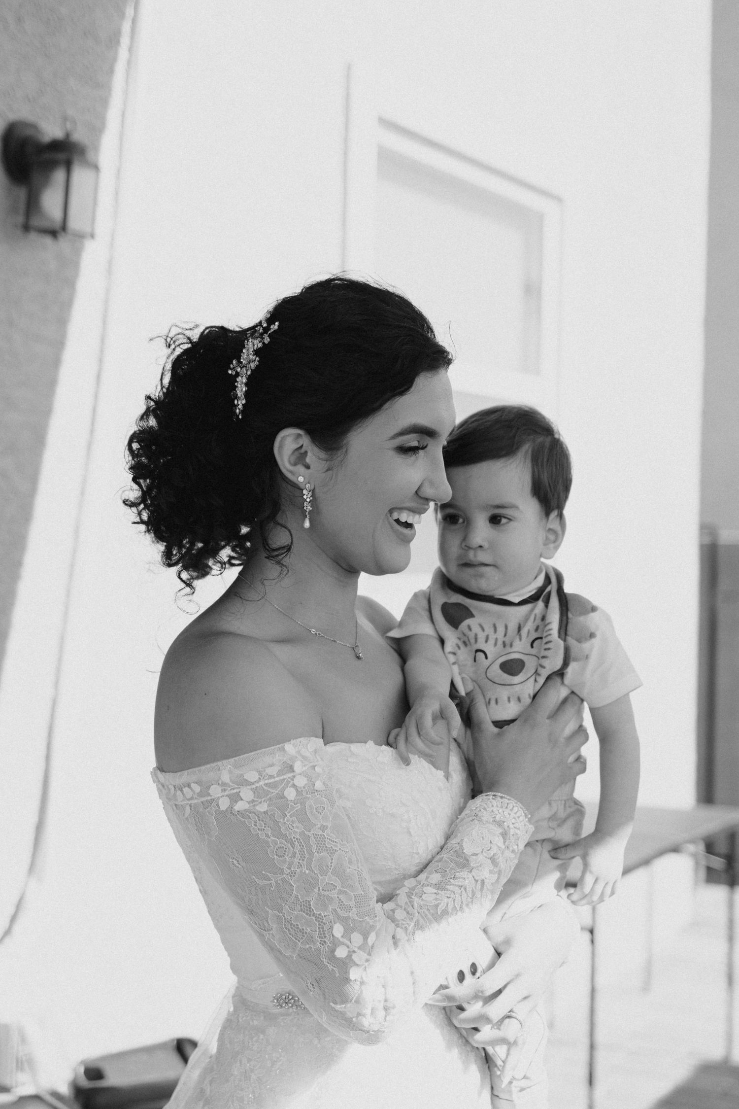 A bride in a strapless wedding dress shares a joyful moment with a young child in black and white photography.