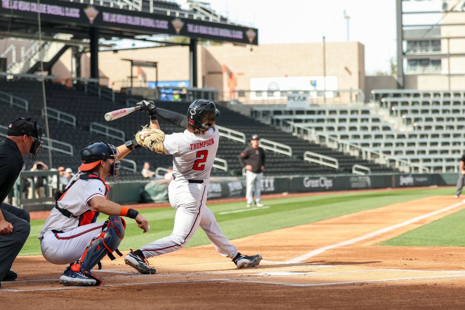 A professional baseball player at bat swings at a pitch during a baseball game at a stadium while the catcher crouches behind home plate.