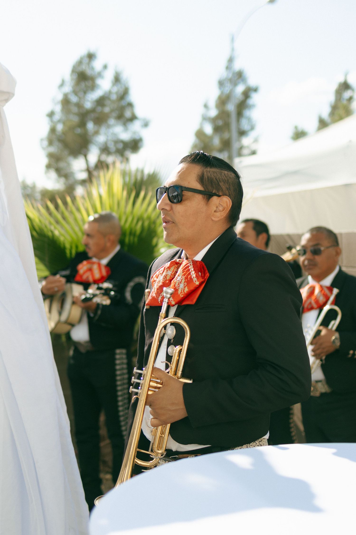 Mariachi band in black suits with red ties performing at an outdoor wedding celebration.
