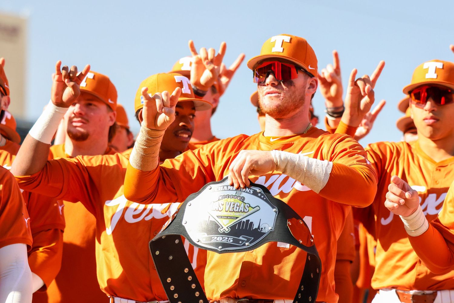 Enthusiastic sports fans in bright orange jerseys celebrate together holding a championship trophy while cheering outdoors.