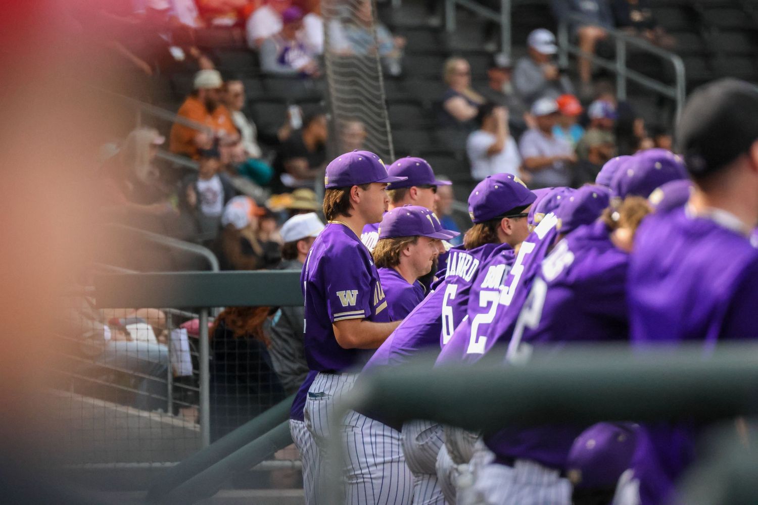 Baseball players in purple uniforms gather in the dugout during a game at a professional baseball stadium.